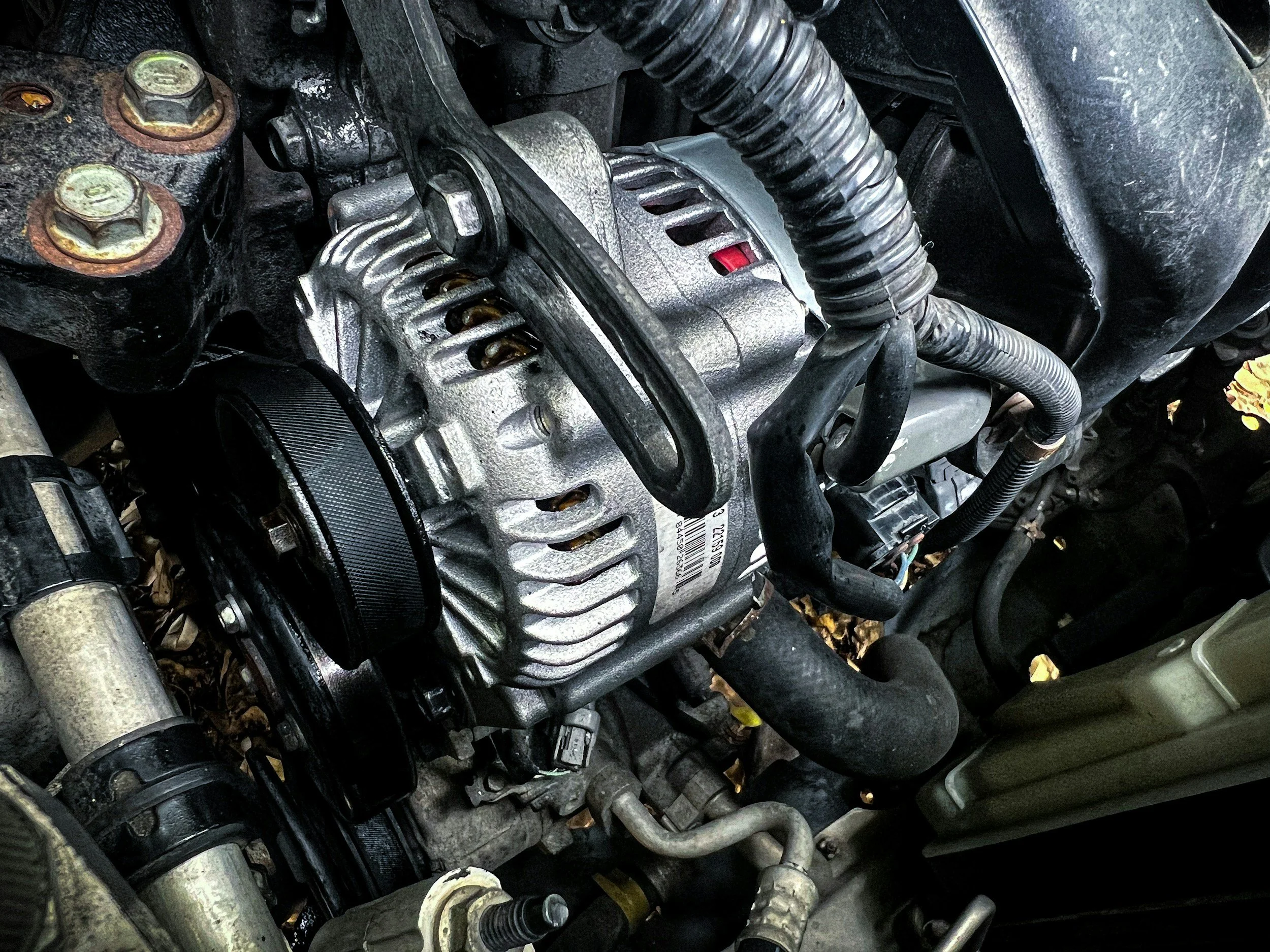 Close-up of a car engine with various metal parts, hoses, and wires, showing signs of dirt and use.