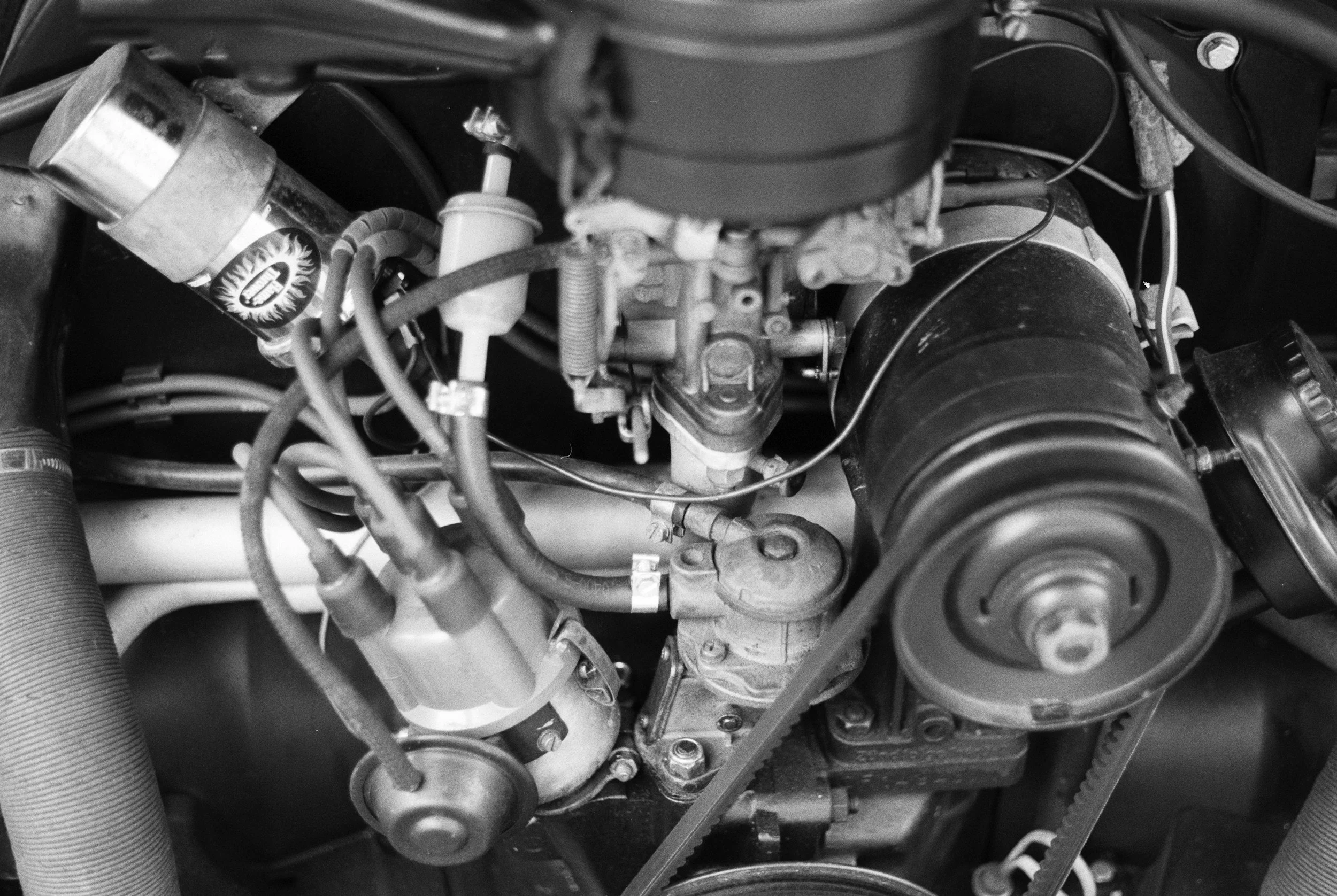 Black and white photo of a car engine showing various mechanical components, hoses, and belts.