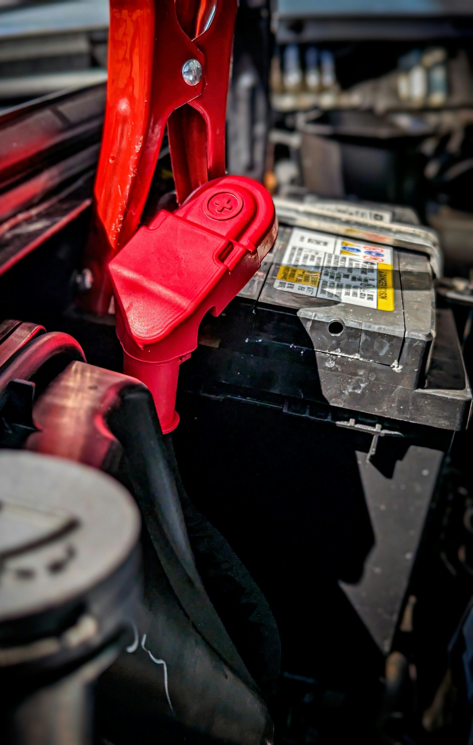 Close-up view of a red battery terminal cover attached to a car battery in an engine compartment.