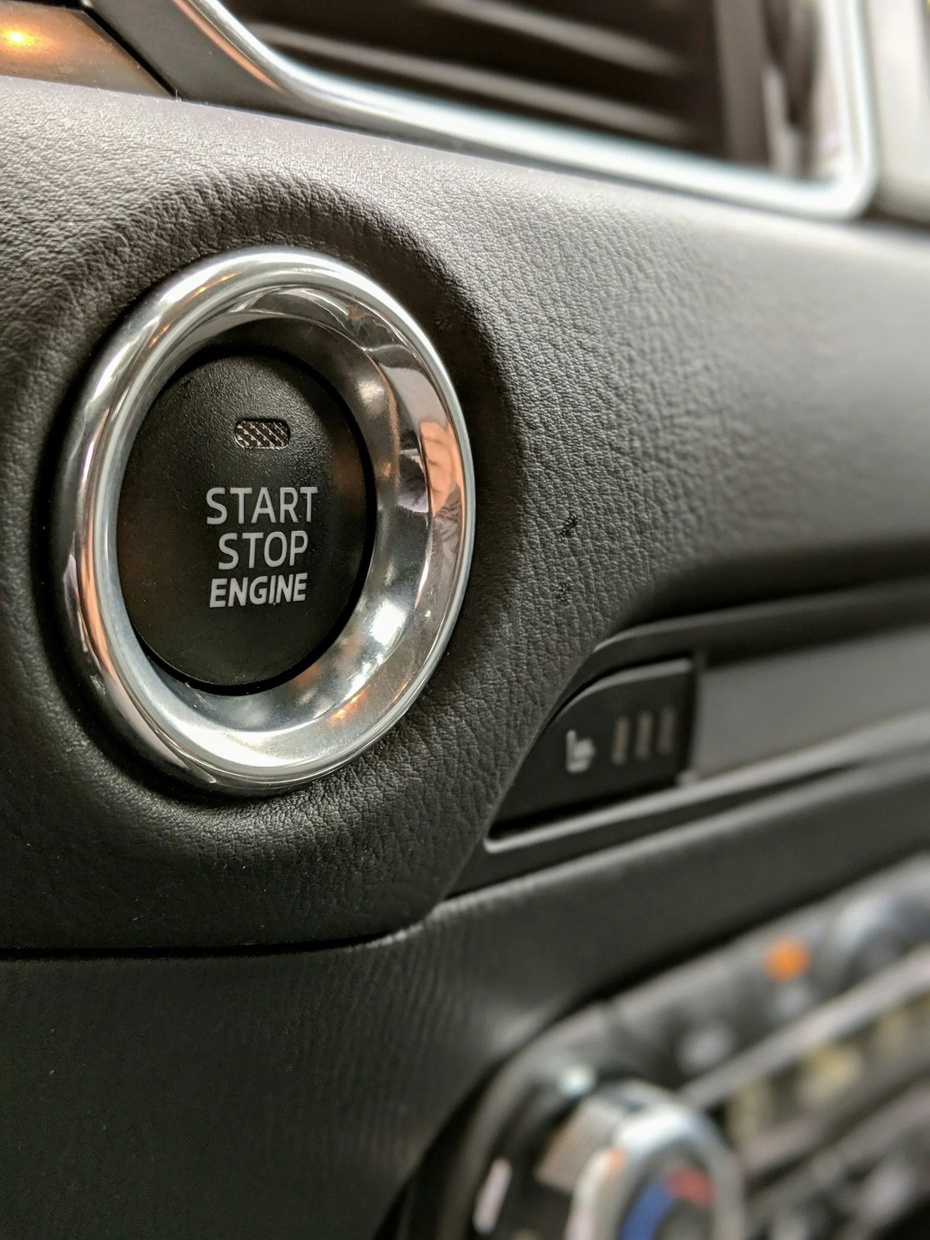 Close-up of a car engine start/stop button with metallic trim, situated on a textured dashboard.