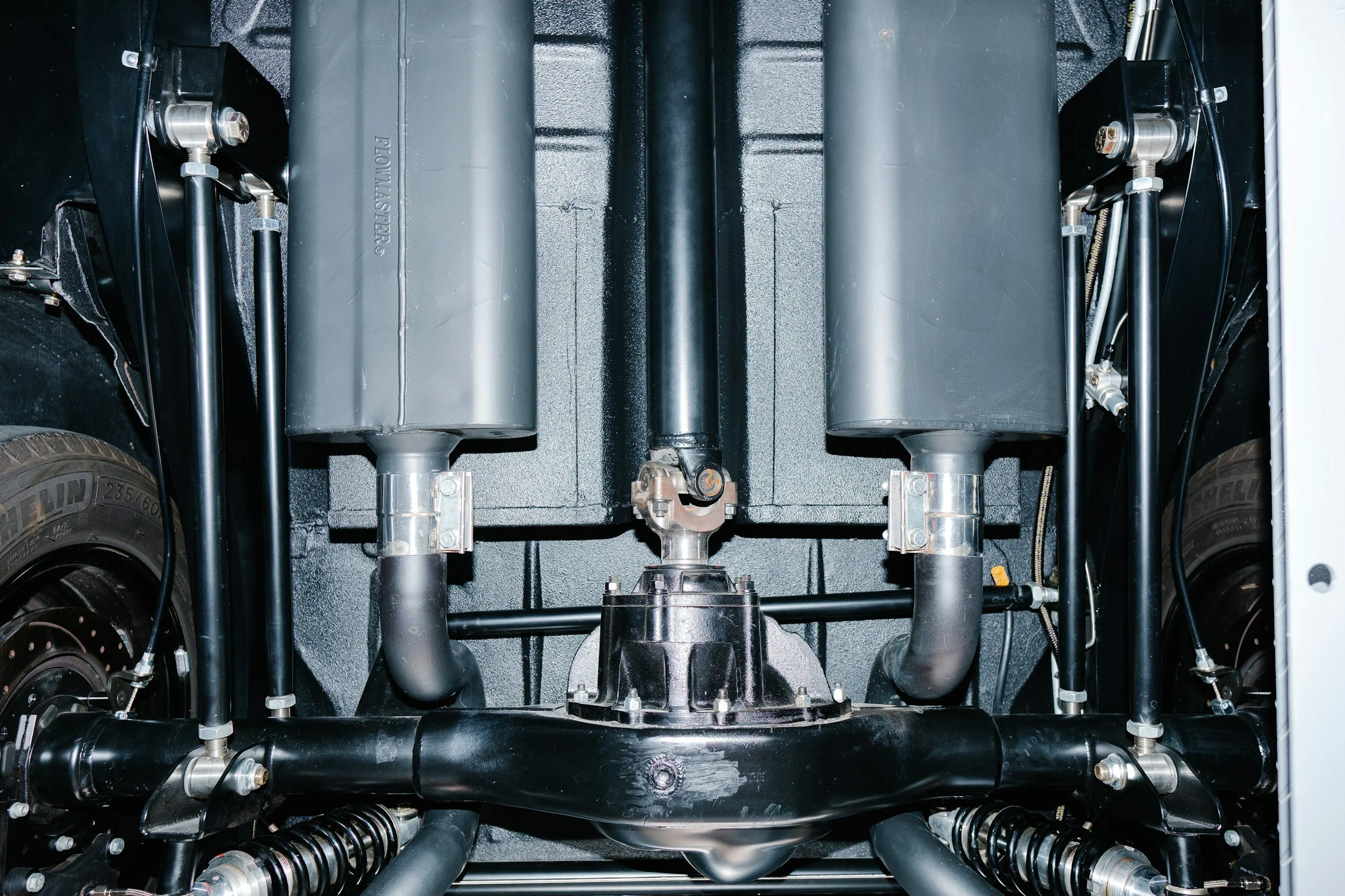 View of an engine bay showing black hoses, pipes, and two large gray cylindrical components.