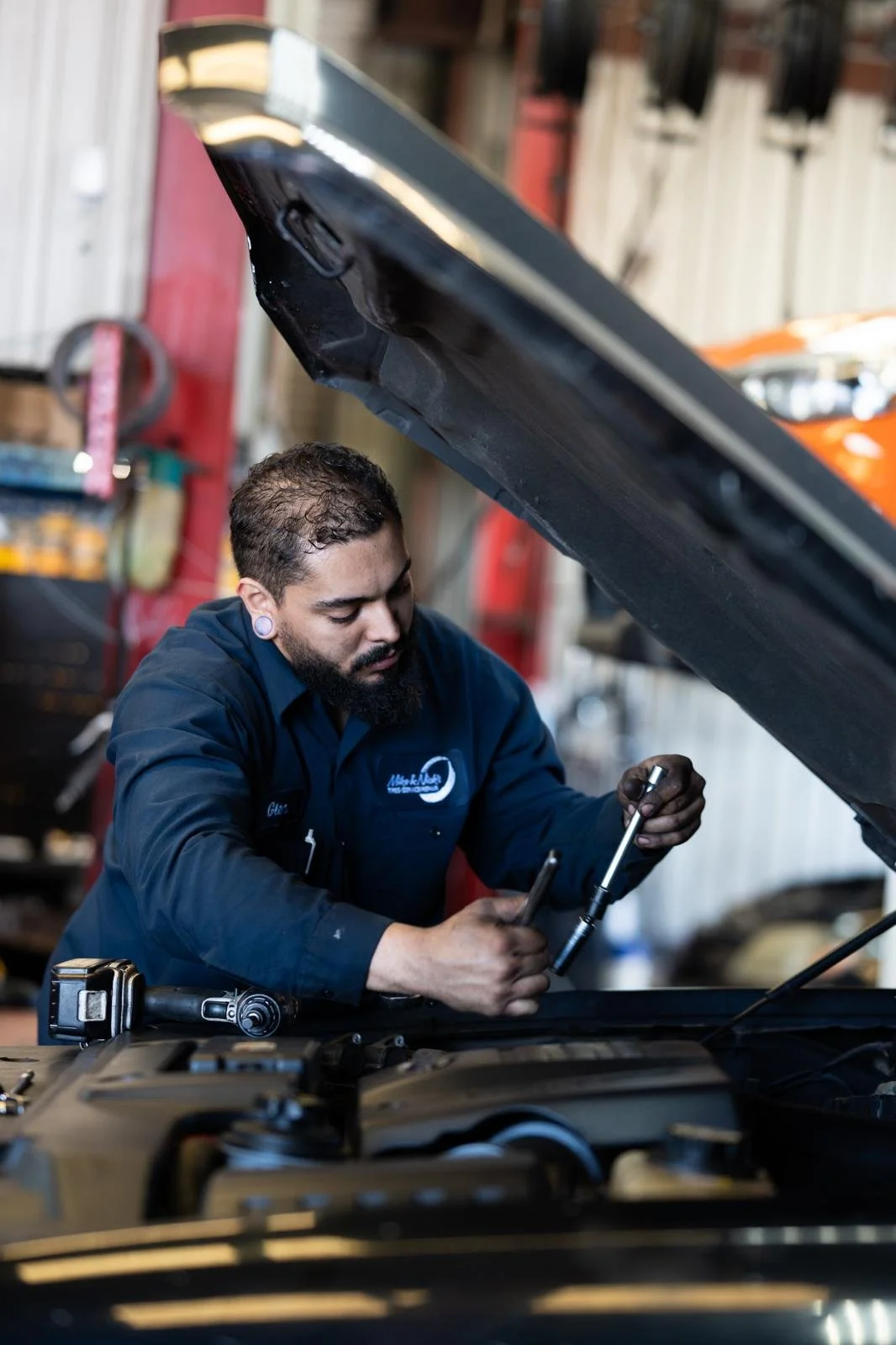 A mechanic is working under the open hood of a car in a garage.