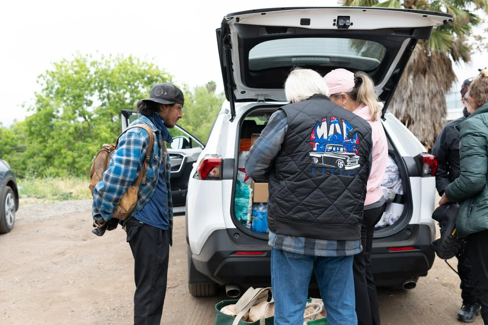 Group of people loading outdoor gear into the trunk of a white SUV in a natural setting with trees, preparing for an outdoor activity.