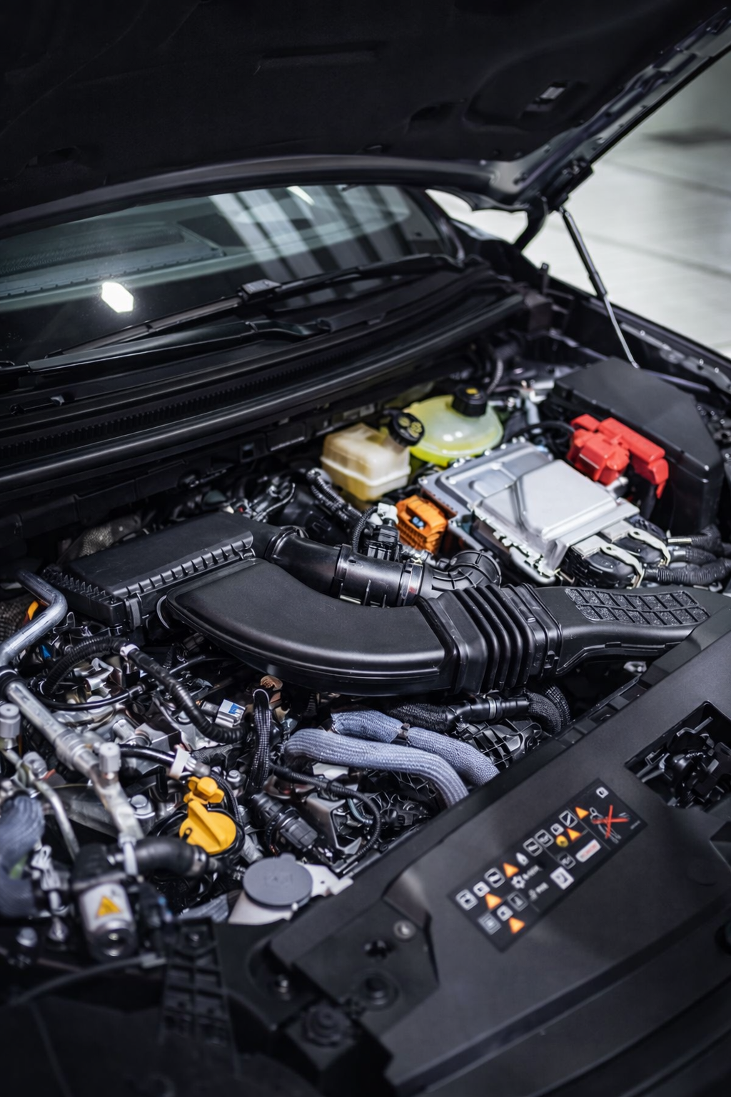 Close-up view of a car engine bay, showing various engine components, hoses, and fluid reservoirs under an open hood.
