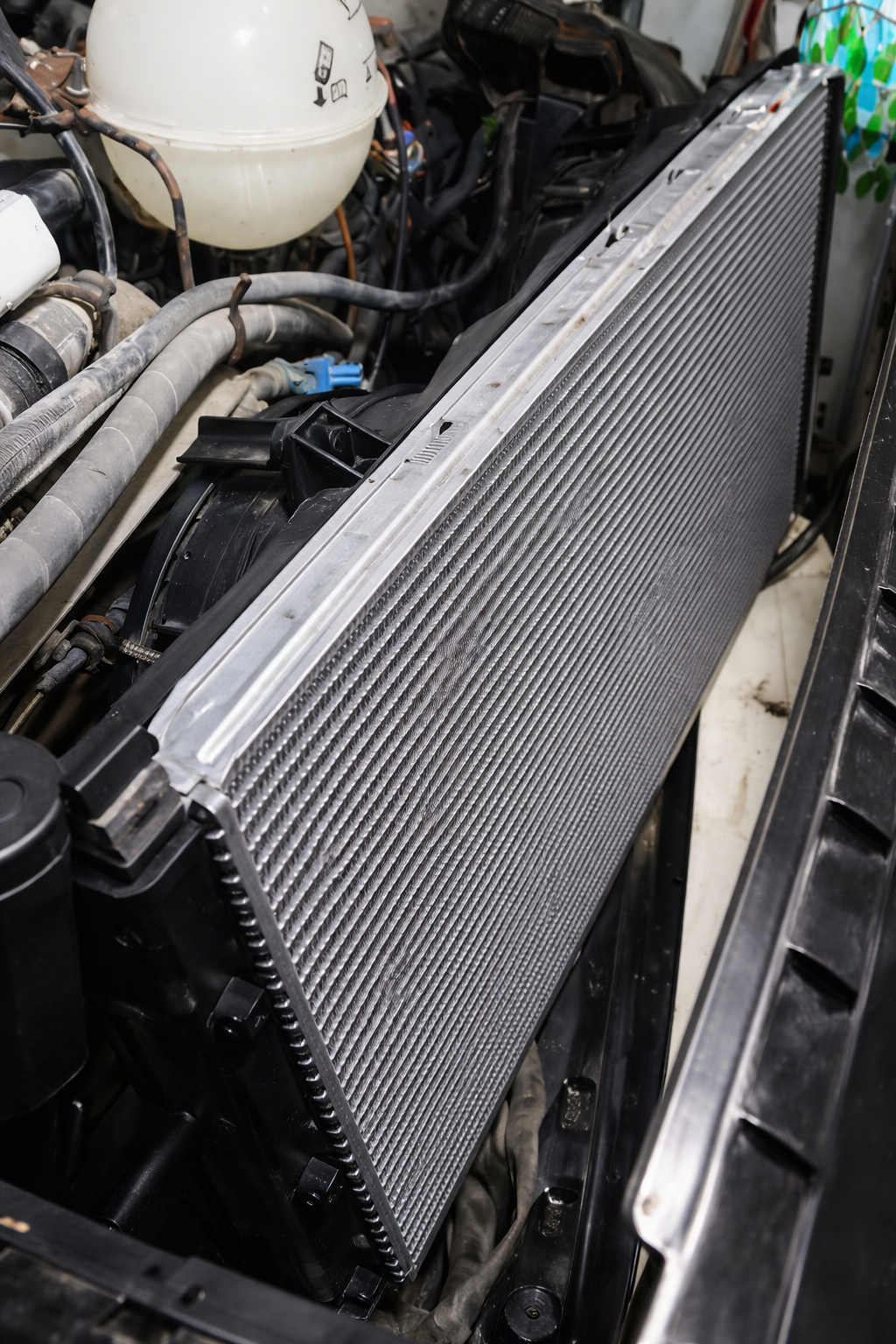 Close-up of a car radiator installed in an engine bay with various hoses and components surrounding it.