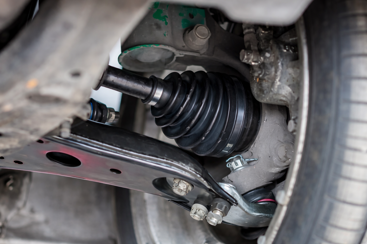 Close-up of a vehicle's suspension system showing a black rubber CV joint boot, driveshaft, and metal mounting components.
