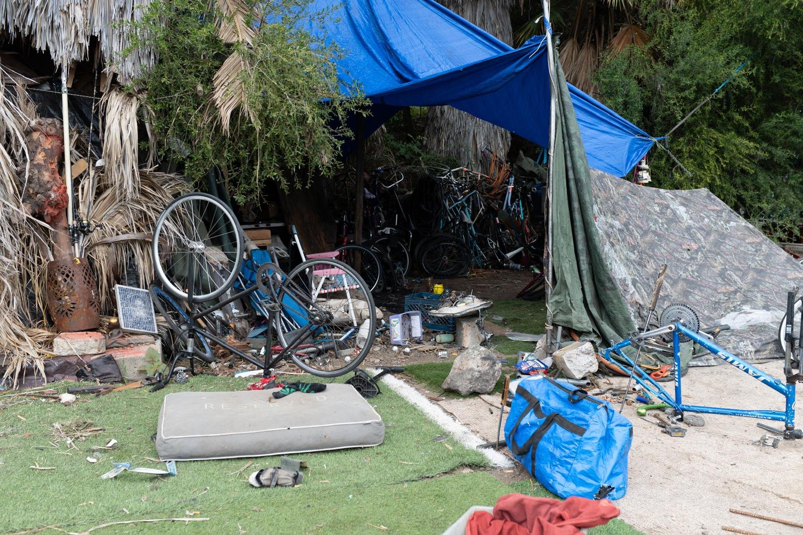 Disorganized outdoor area with bicycles, rocks, luggage, and tarps.