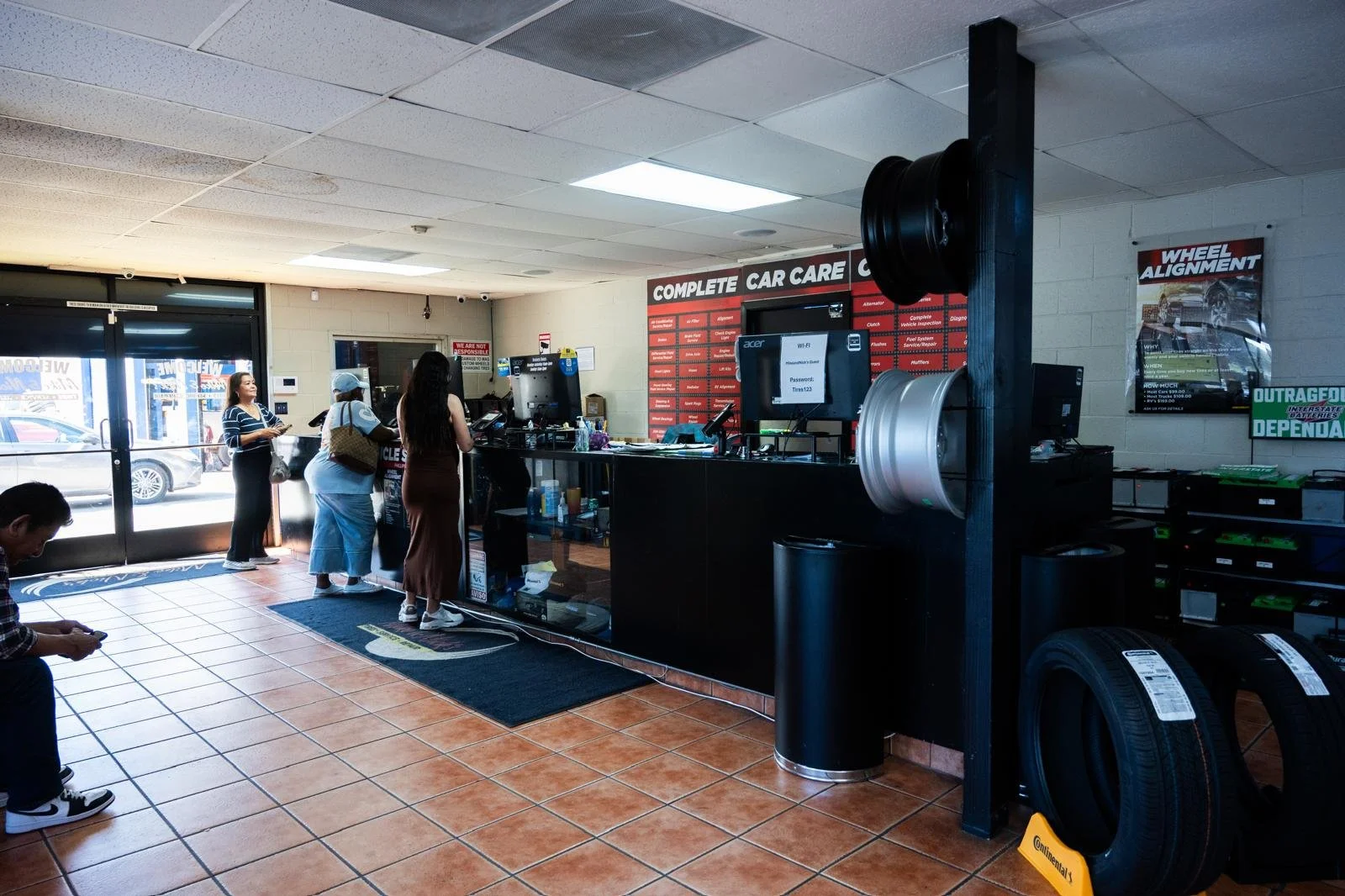 Inside of an automotive service center with customers at the service counter, tires on display, and tire change equipment.
