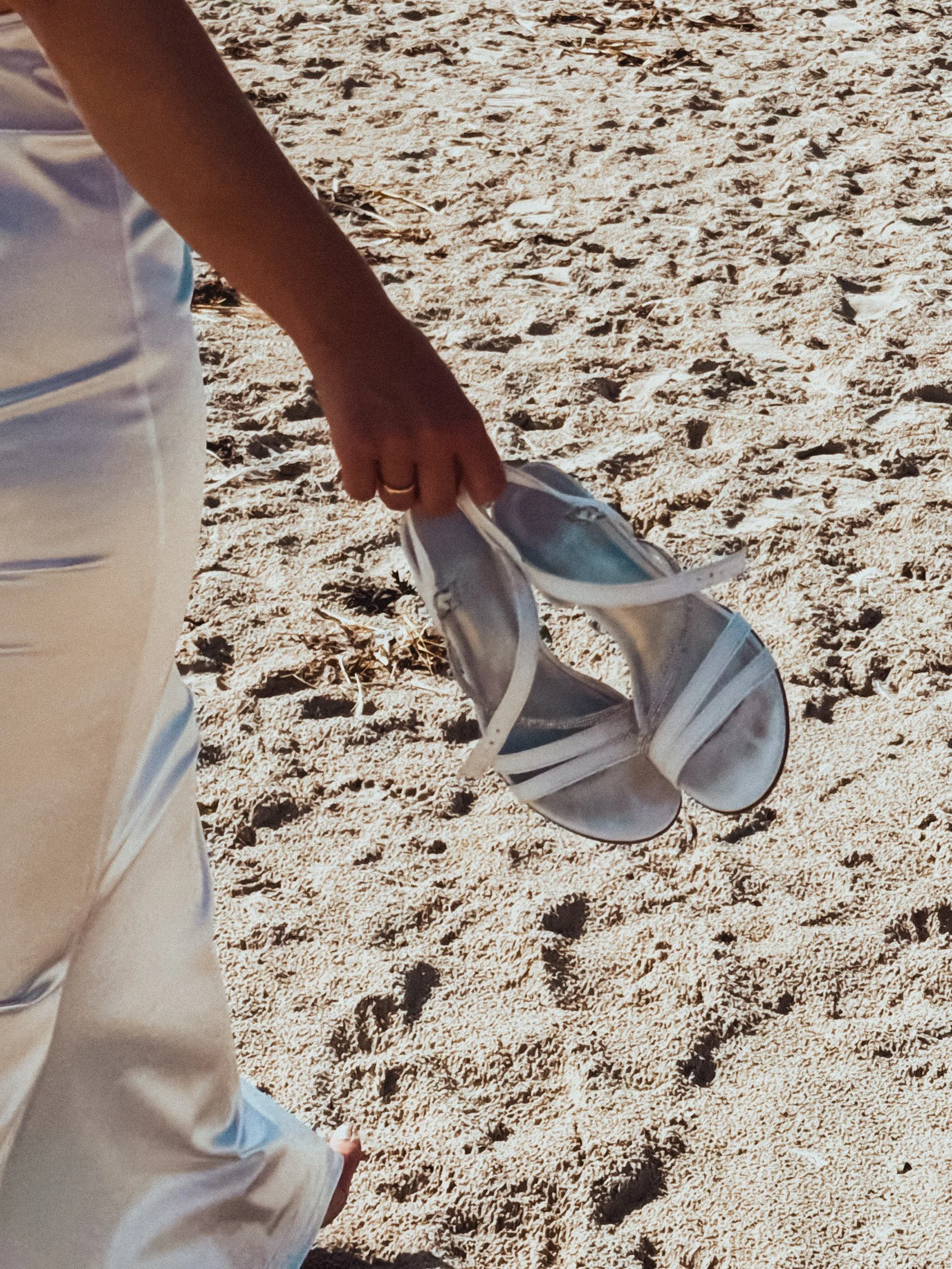 Braut läuft barfuß am Strand und trägt weiße Sandalen in der Hand