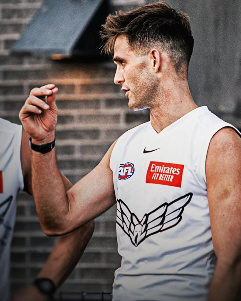 Sam Glover in an Australian Football League jersey with an AFL logo, Emirates logo, and a hawk emblem.
