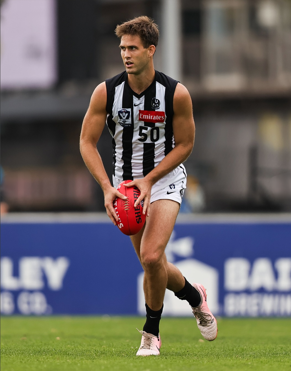 A male athlete playing Australian rules football, wearing a black and white striped jersey with the number 50, holding a red football, on a grass field.