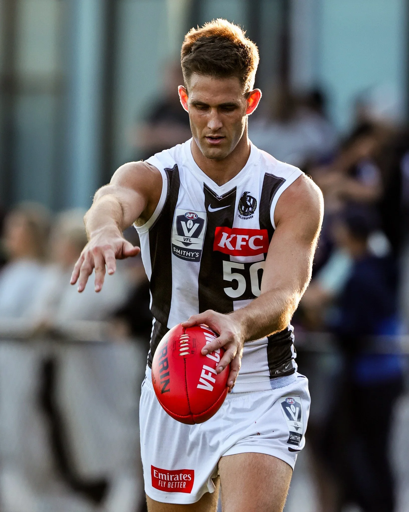 A young male athlete in a black and white sports uniform with various sponsor logos, holding a red football, during an Australian rules football game.