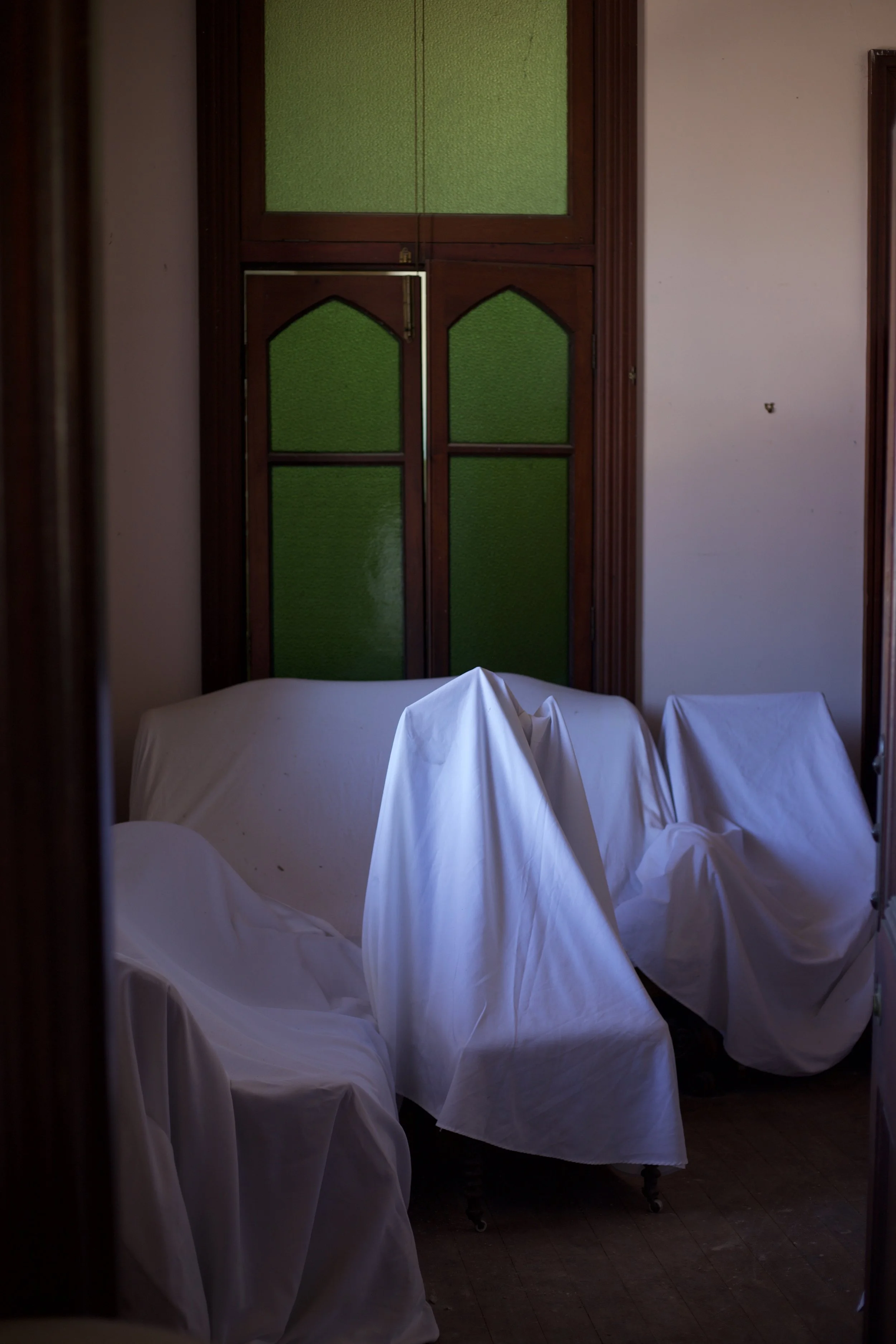Empty chairs covered with white cloths in a room with wooden framed green glass windows.