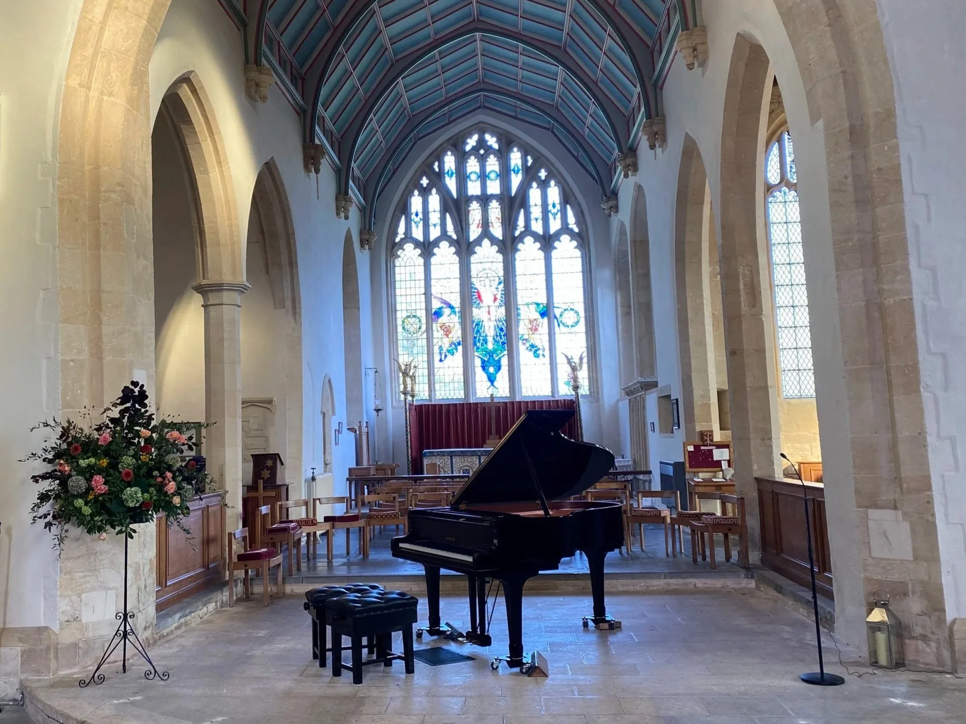 Piano in Church with large stained glass window behind it.
