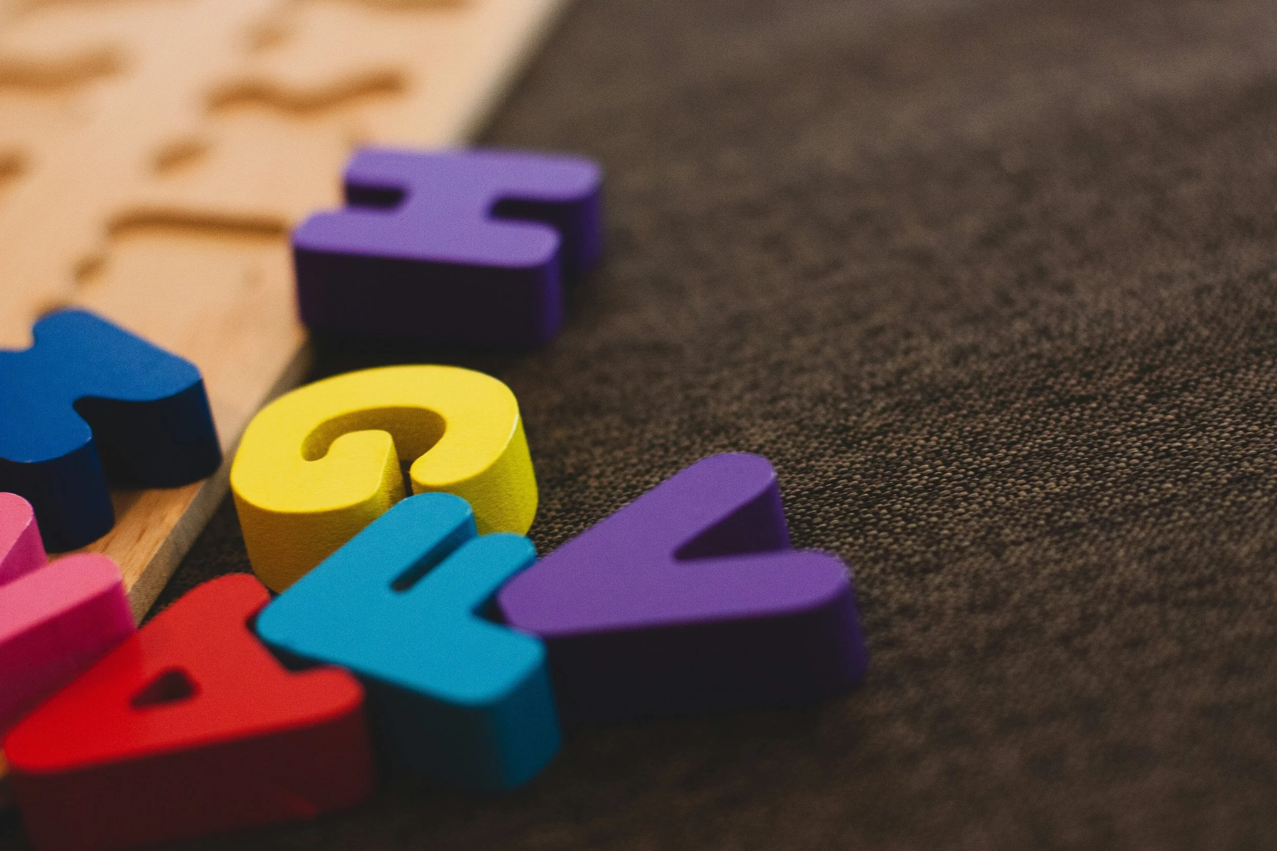 Close-up of colorful letter and number blocks on dark fabric surface, with focus on purple and yellow blocks.