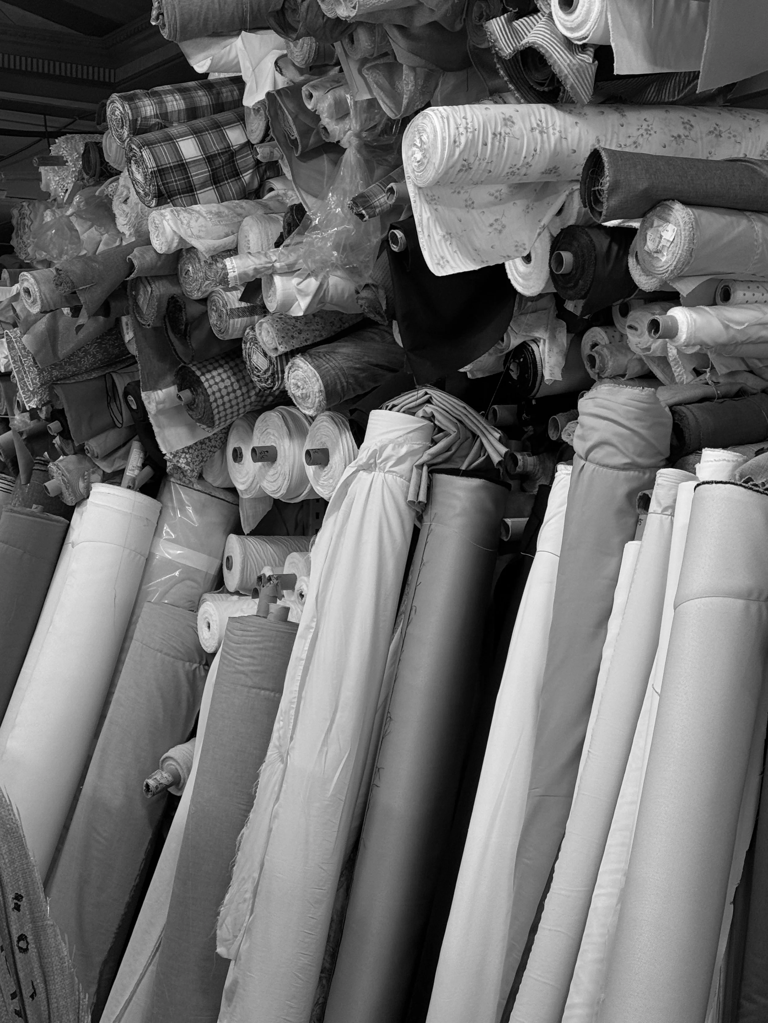 Stacks of fabric bolts and rolls in various patterns and textures, organized on shelves or tables.