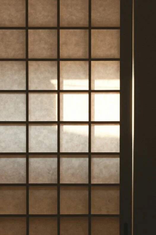 A shoji-style window with a lattice grid, allowing sunlight to pass through and cast shadows inside.