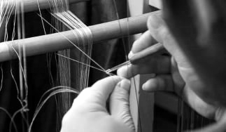 A person weaving thread on a loom with their hands