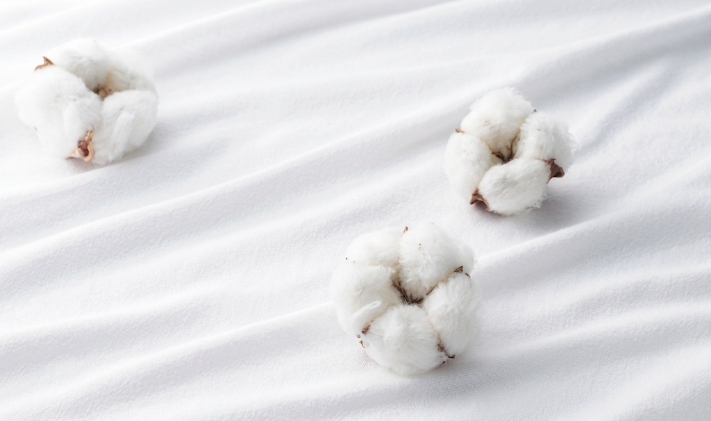 Three cotton bolls on a white fabric background.