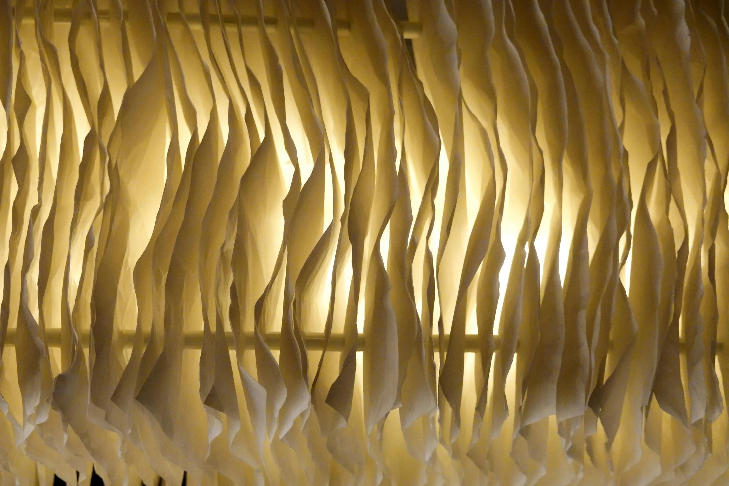 Close-up view of a textured, illuminated, folded-paper or fabric surface with a warm yellow glow.