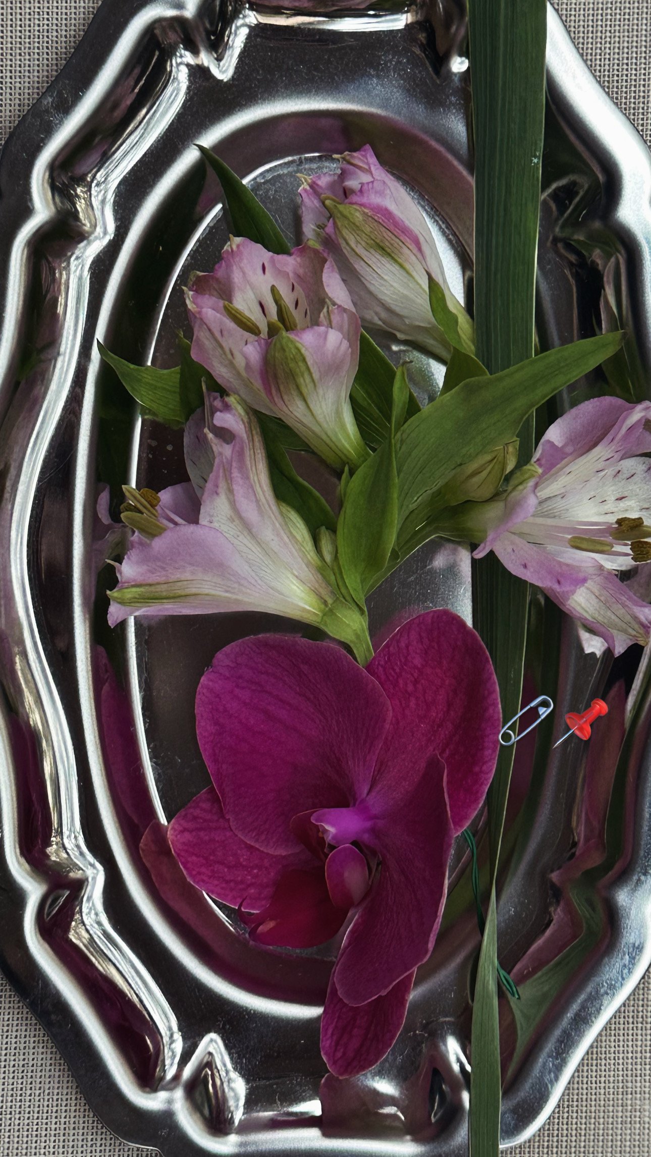 A silver platter with pink and white flowers and a dark pink flower, with a green leaf and pin.