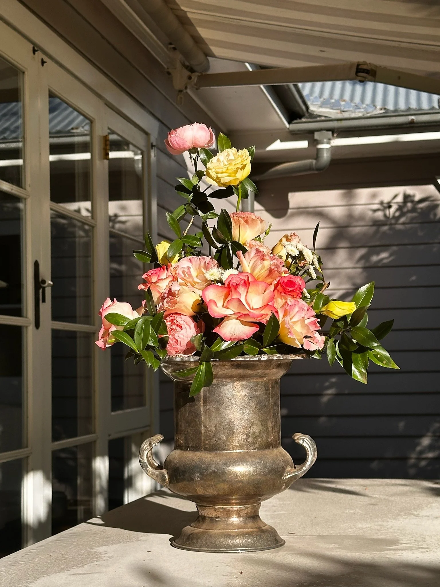 A vintage champagne cooler holding a bouquet of pink, yellow, and cream-colored roses with green leaves. 