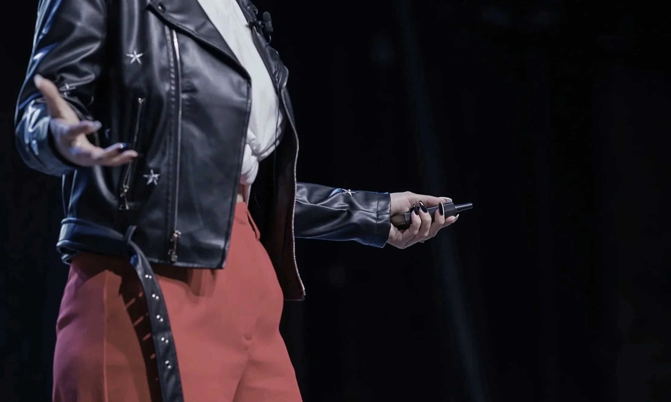 Person wearing a black leather jacket with star accents, holding a cellphone in their right hand, against a dark background.