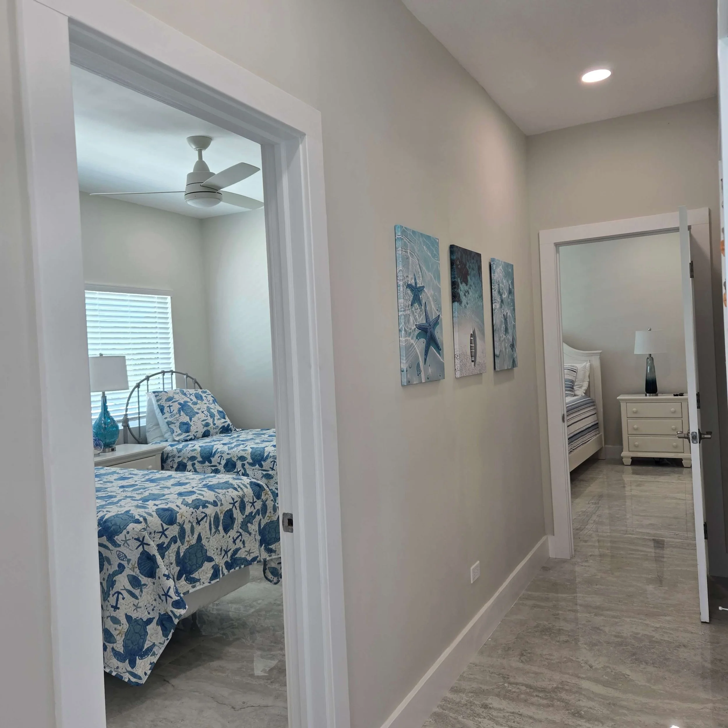 Bedroom with a bed that has a blue and white ocean-themed bedspread, window with blinds, and framed ocean-themed artwork on the wall.