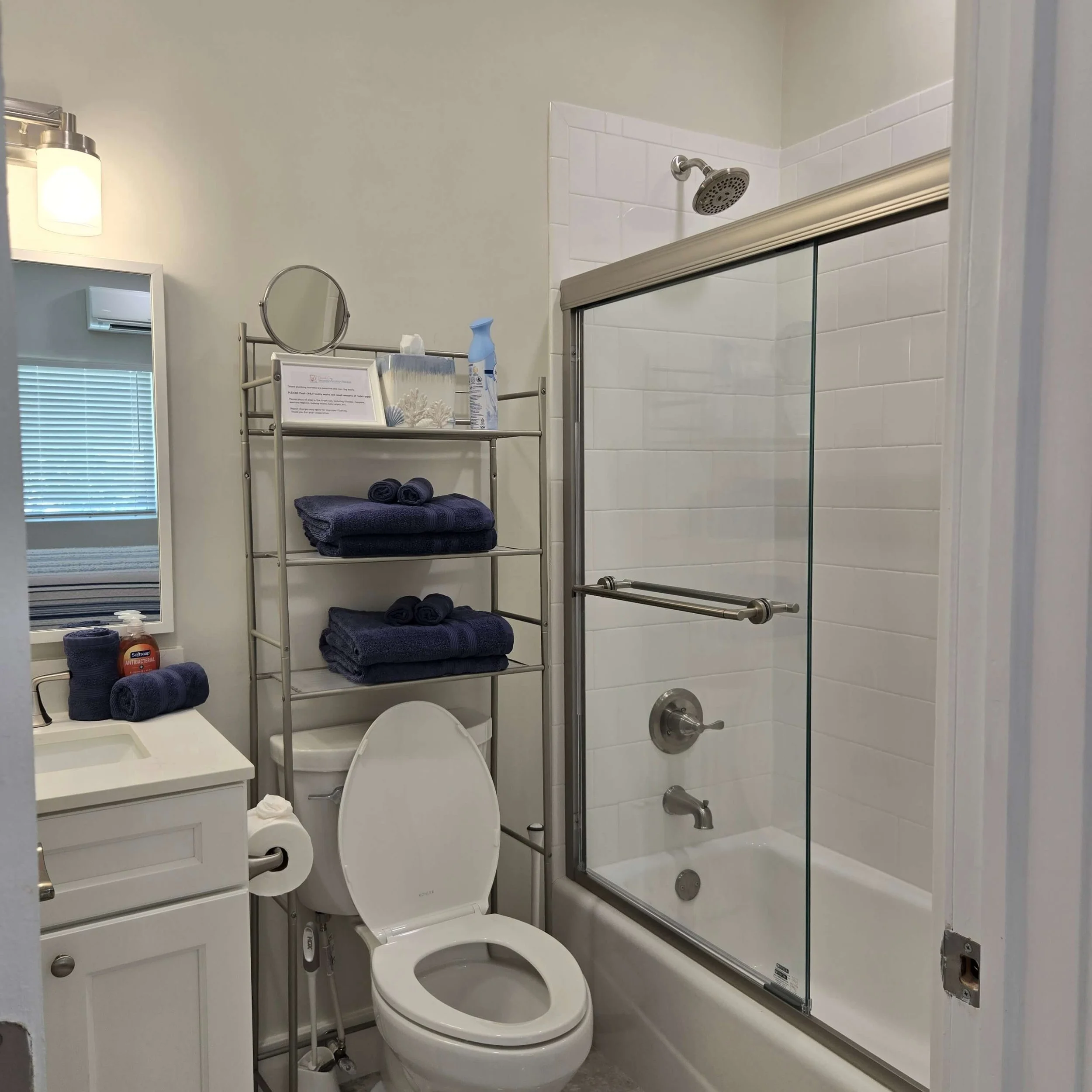 Bathroom with a toilet, a shower with sliding glass doors, a mirror, and storage shelves with towels and toiletries.
