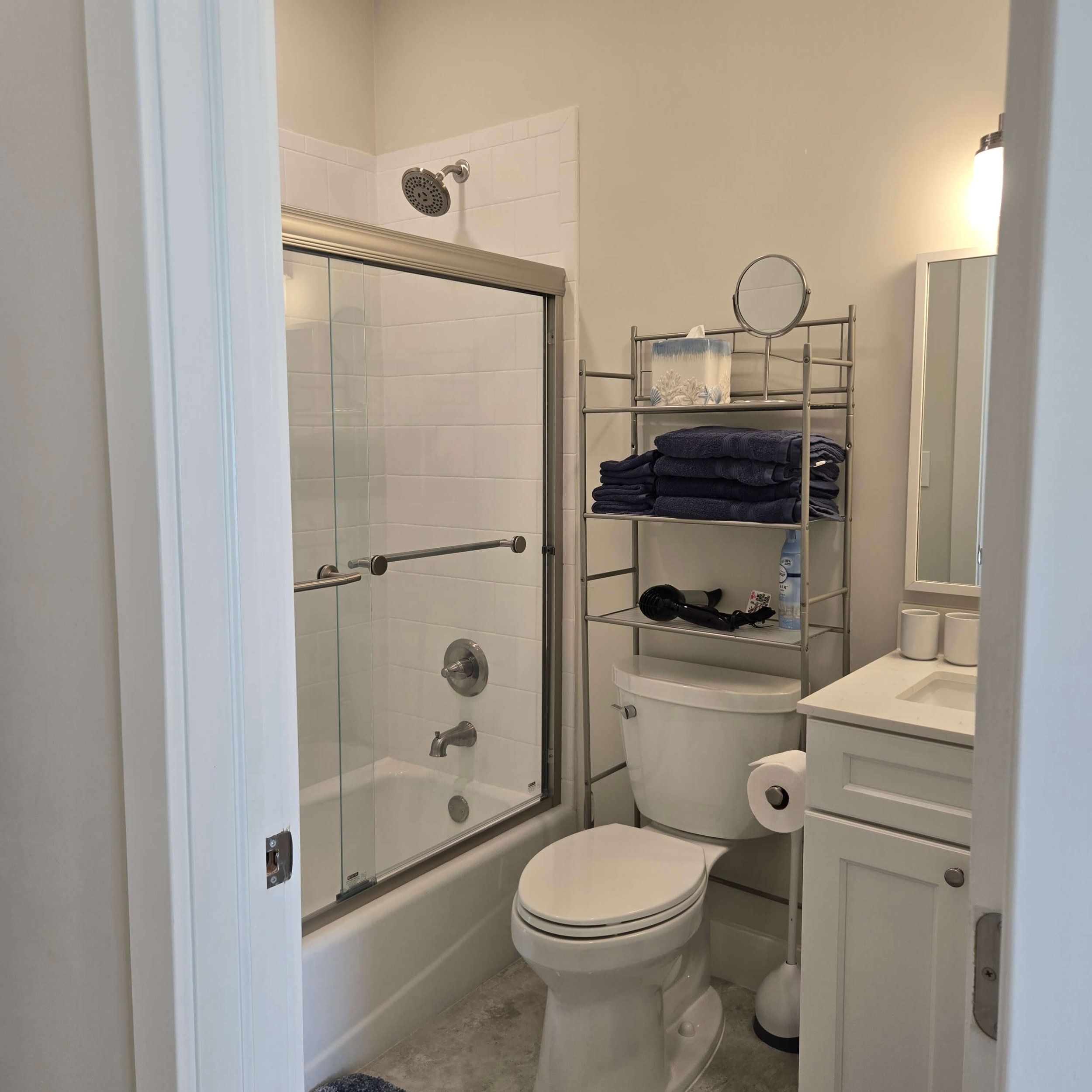 Bathroom with shower, toilet, and bathroom storage shelves with folded towels and personal care items.