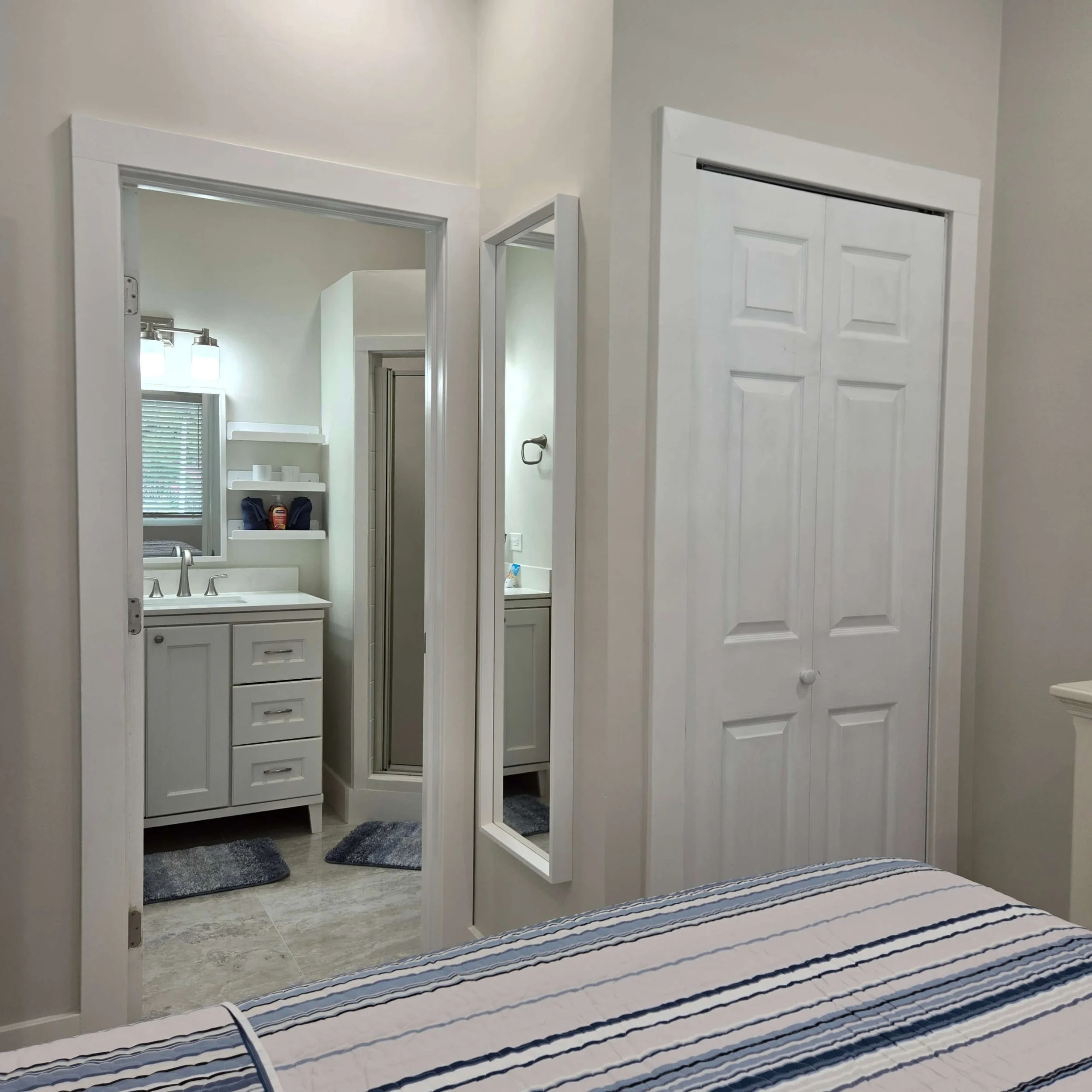 View of a bedroom with a large mirror, a bathroom vanity with a sink, and construction animal-shaped rugs on the floor, as seen from above a bed with a striped blanket.