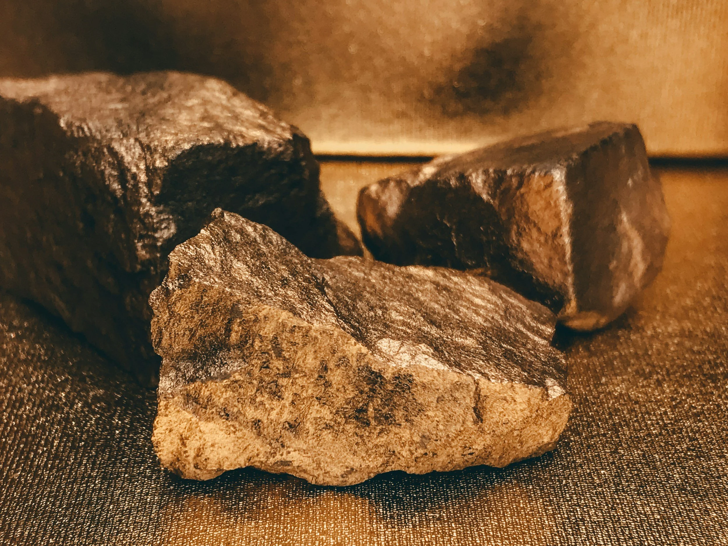 Close-up of three dark, rough, irregularly shaped stones on a textured brown surface.