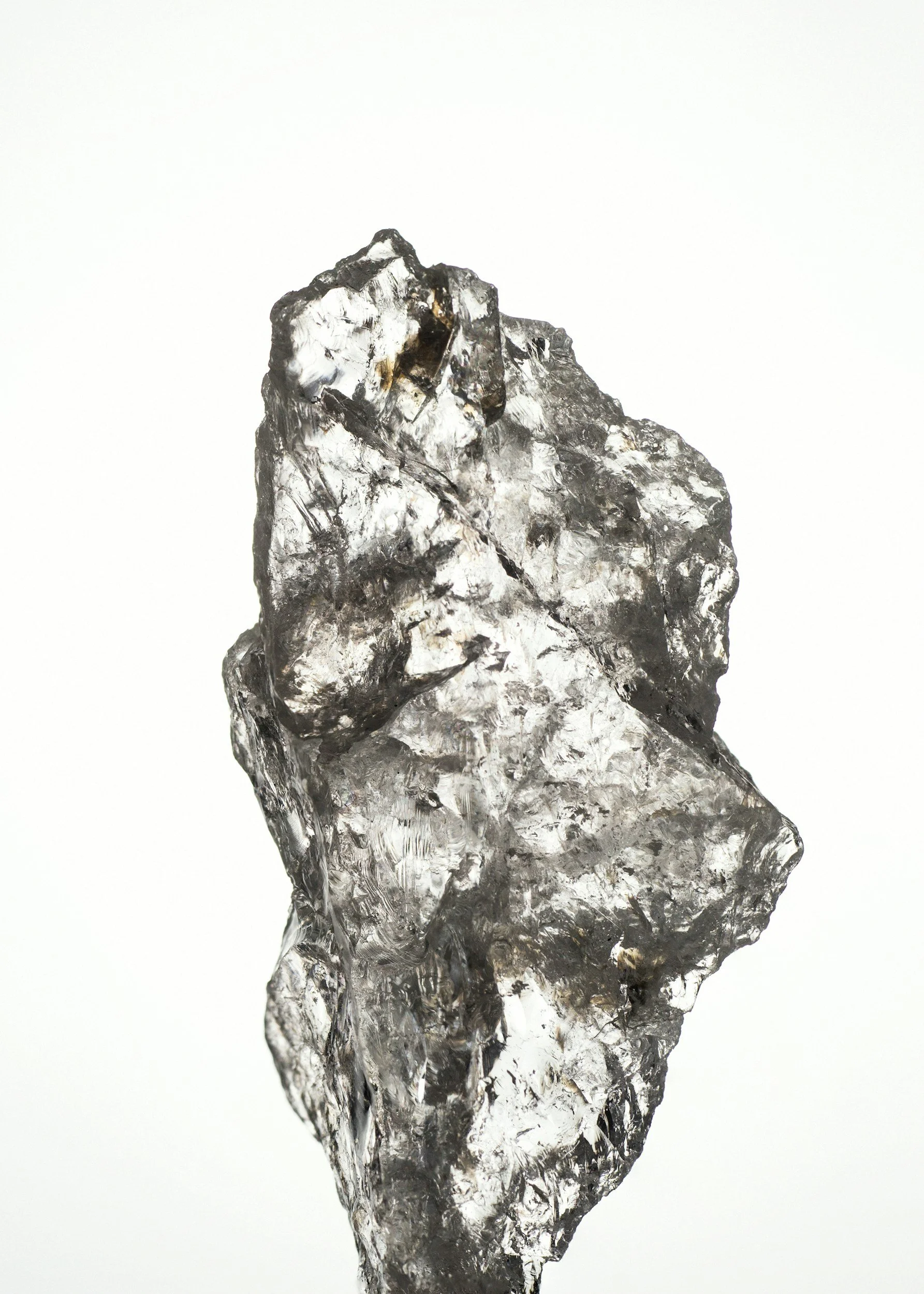 A clear, roughly triangular piece of obsidian with jagged edges and a shiny, reflective surface.