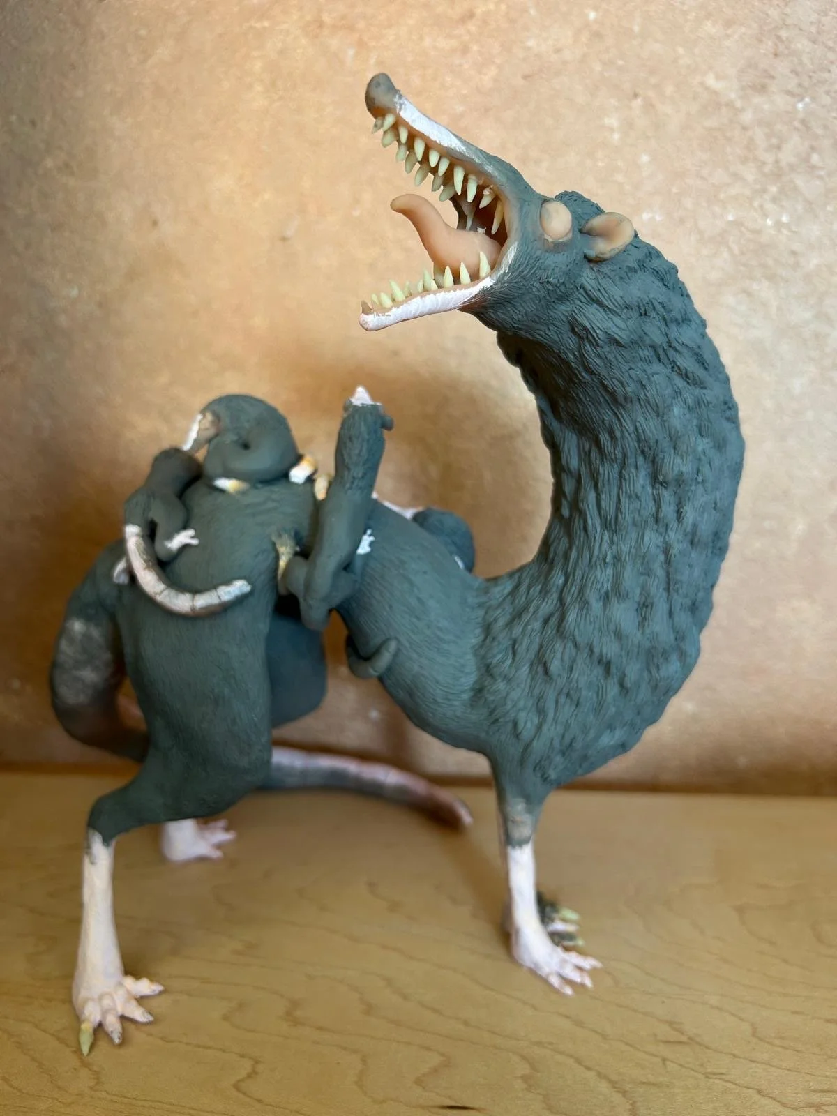 A strange sculpture of a giant opossum with a long neck, open mouth showing sharp teeth, and a foot on a wooden surface.