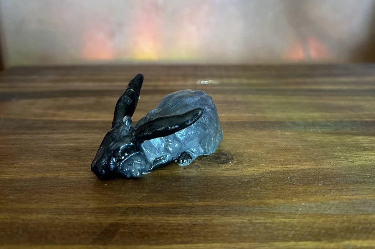 A small, glossy figurine of a black rabbit with long ears, resting on a wooden surface.