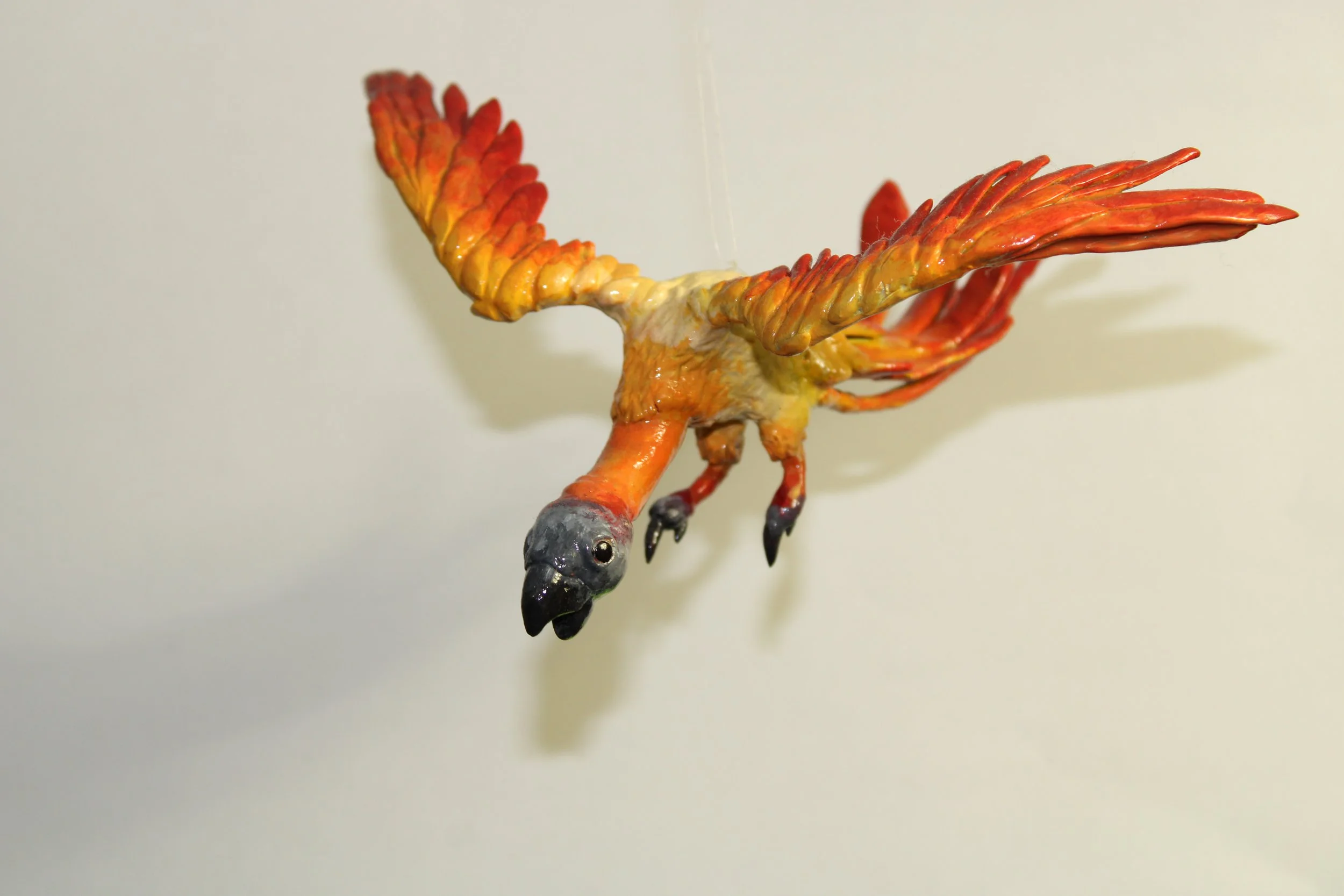 Colorful bird sculpture with red, orange, and yellow feathers, black beak, and gray head.