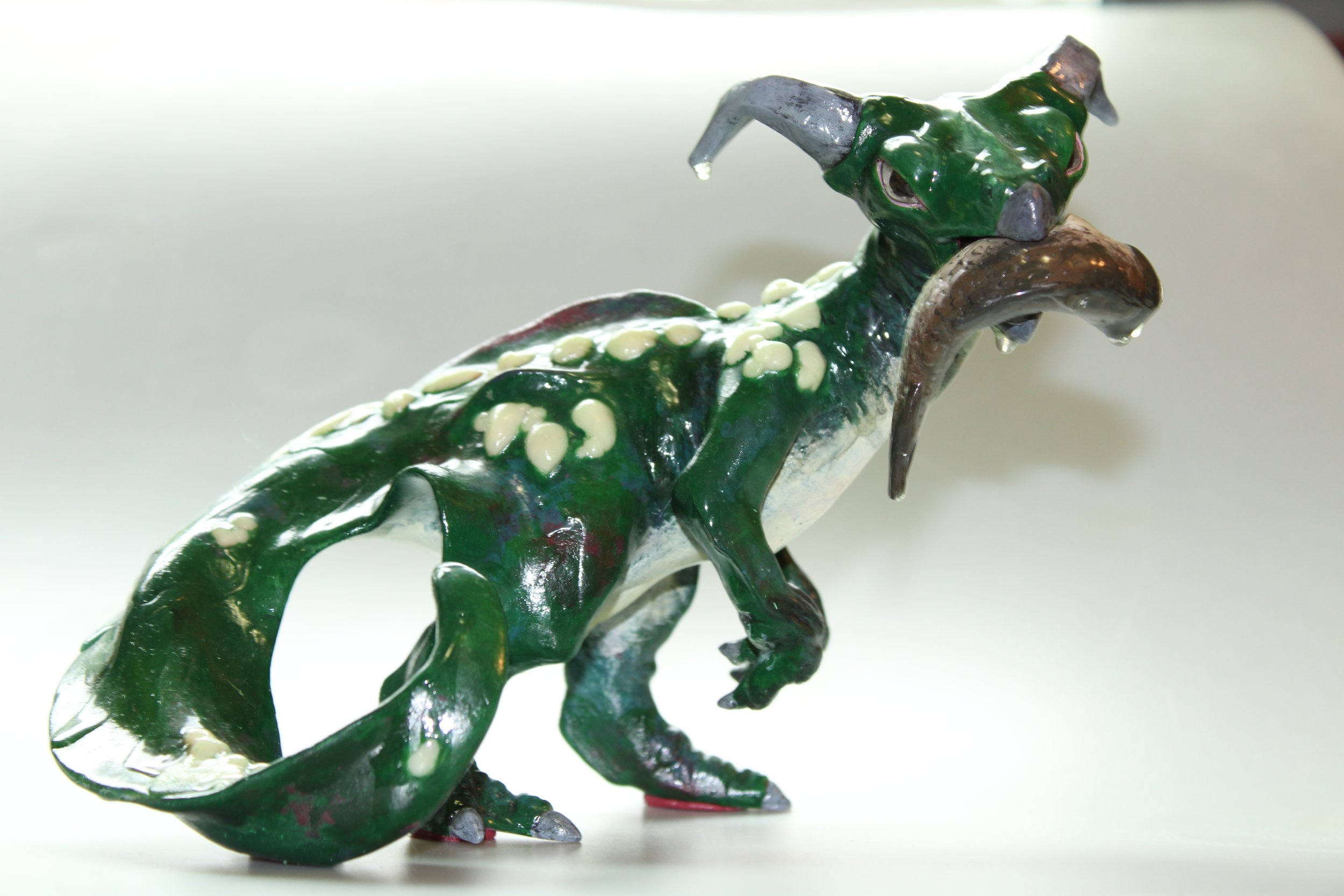 Handmade green dragon sculpture with white spots, horns, and a long tail on a plain white background.
