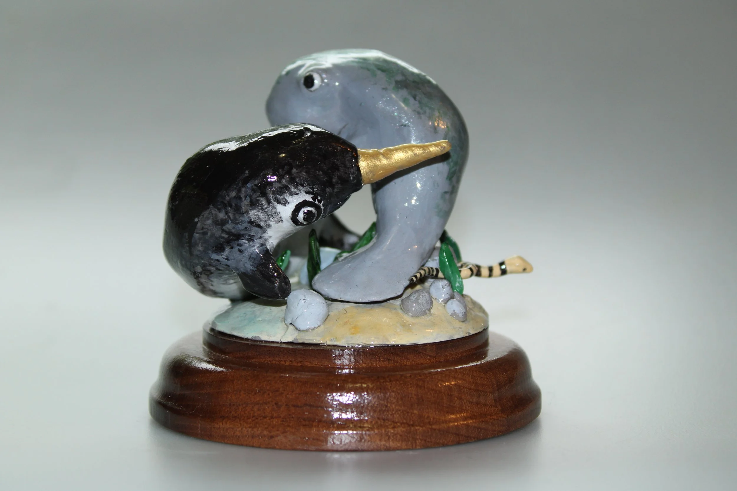 Clay sculpture of a narwhal and a manatee on a wooden base.