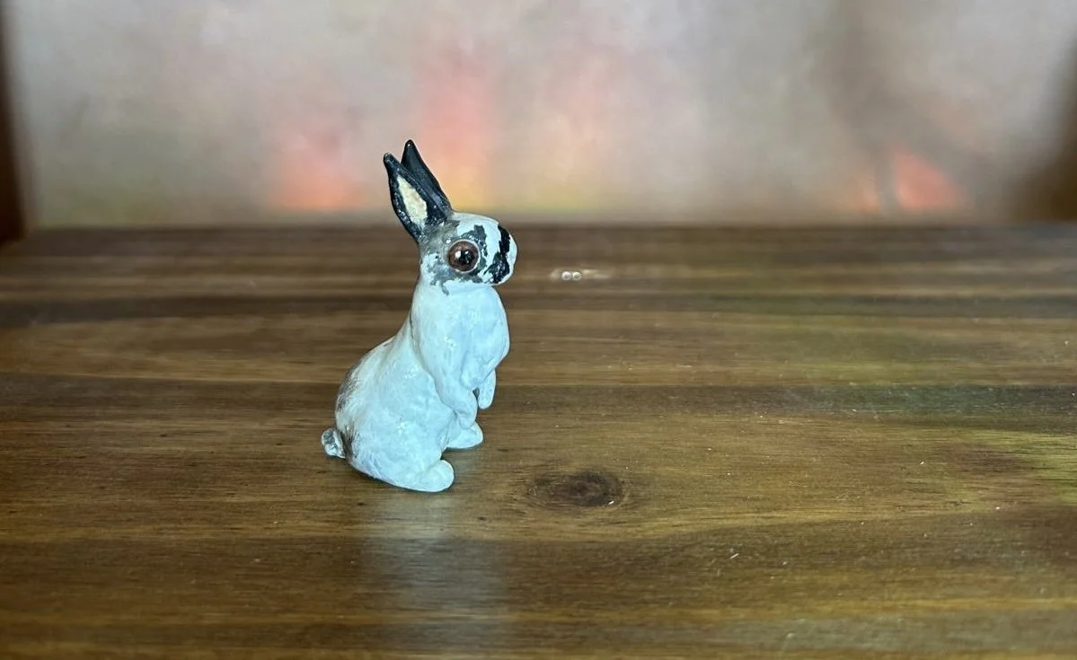 Small rabbit figurine sitting on a wooden surface.