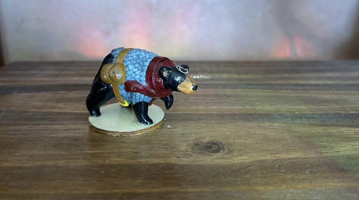 Small figurine of a bear dressed as an adventurer with a pouch and armor, standing on a wooden surface.