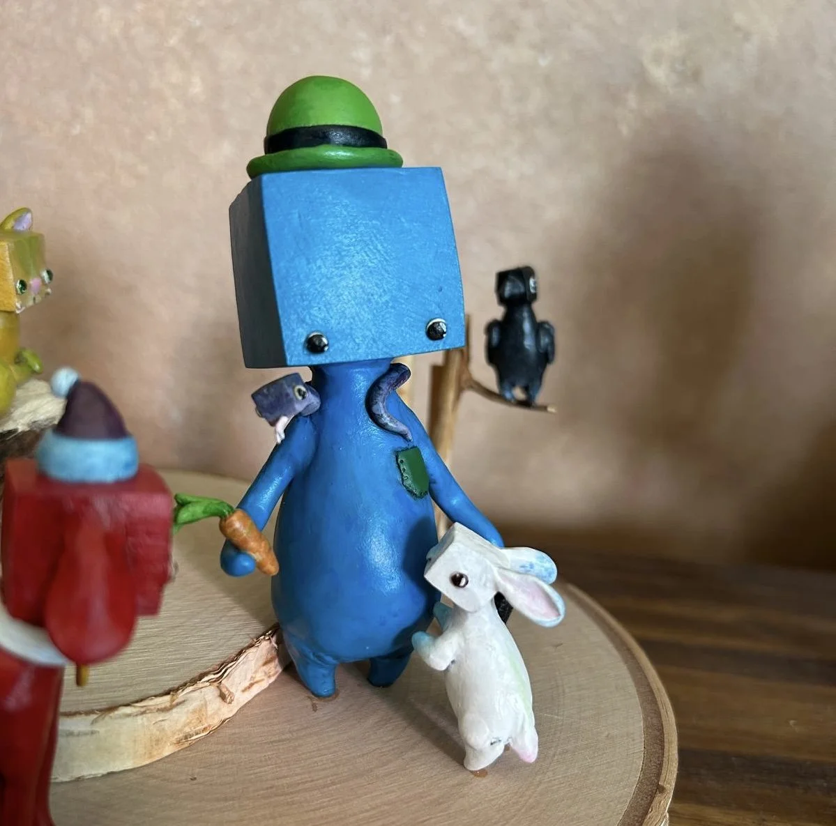 Colorful animal figurines, including a blue one with a green hat and a small white rabbit, arranged on a wooden surface.