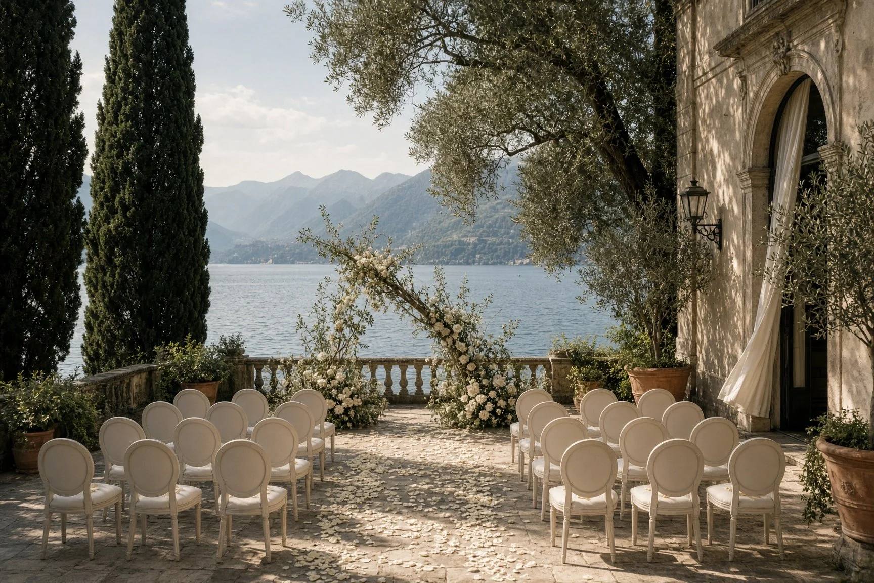 Romantic Lake Como wedding ceremony with ivory chairs, floral arch, olive trees and panoramic lake views at an Italian villa.