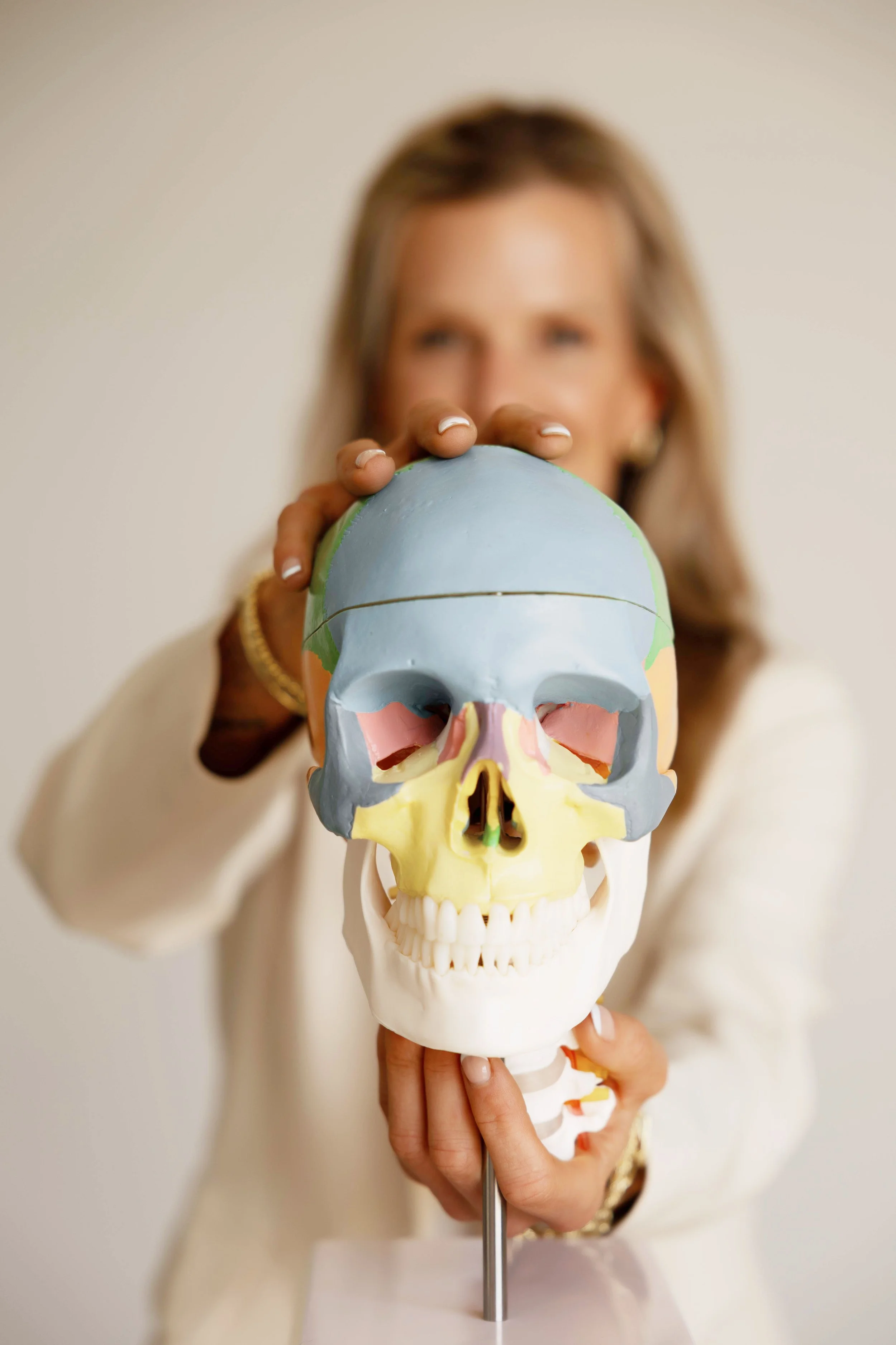 A woman holding a colorful anatomical skull model, extending it toward the camera with a blurred background.