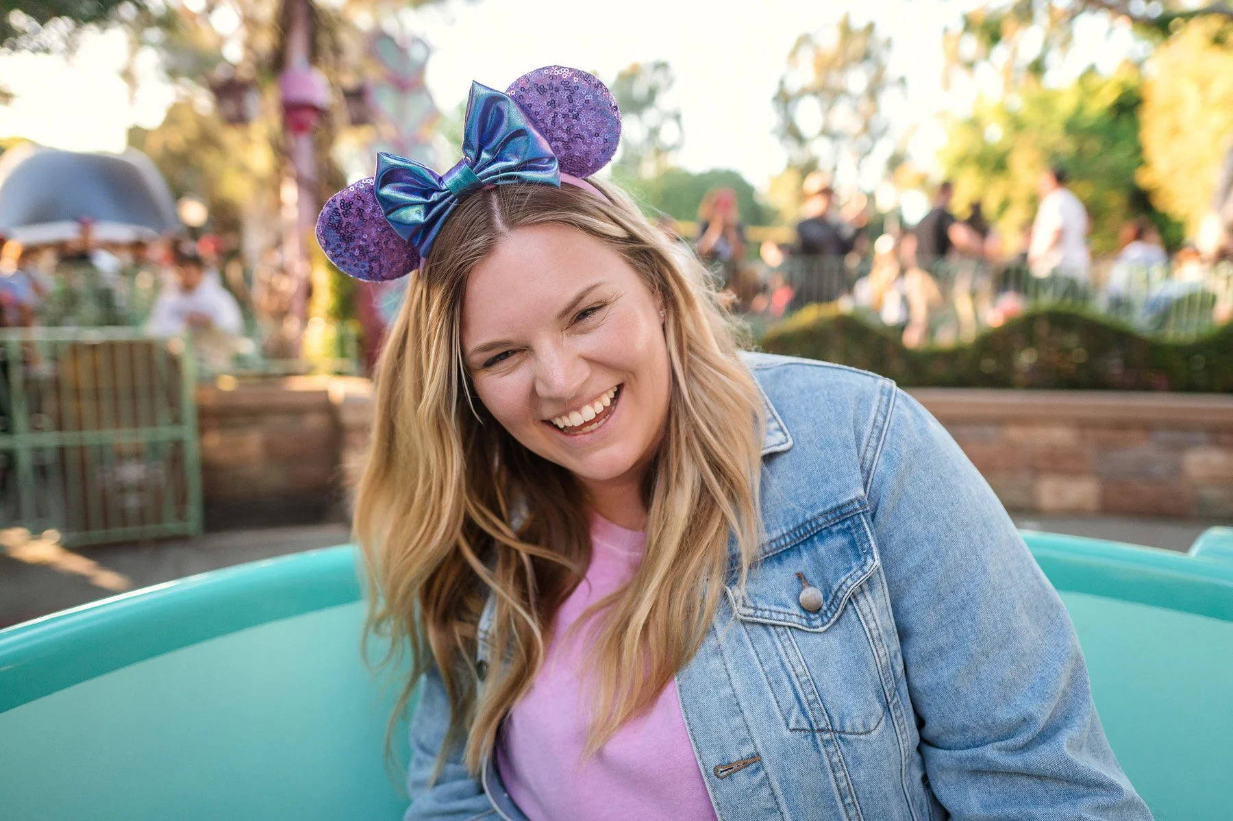 Michelle Hagen. A woman with long blonde hair wearing Disney Mickey ears, smiling outdoors during daytime, with people and trees in the background.
