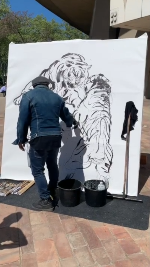 Ramya Chuon en train de dessiner un grand portrait de 2 tigres sur une toile blanche lors d'un événement de live painting en plein air.
