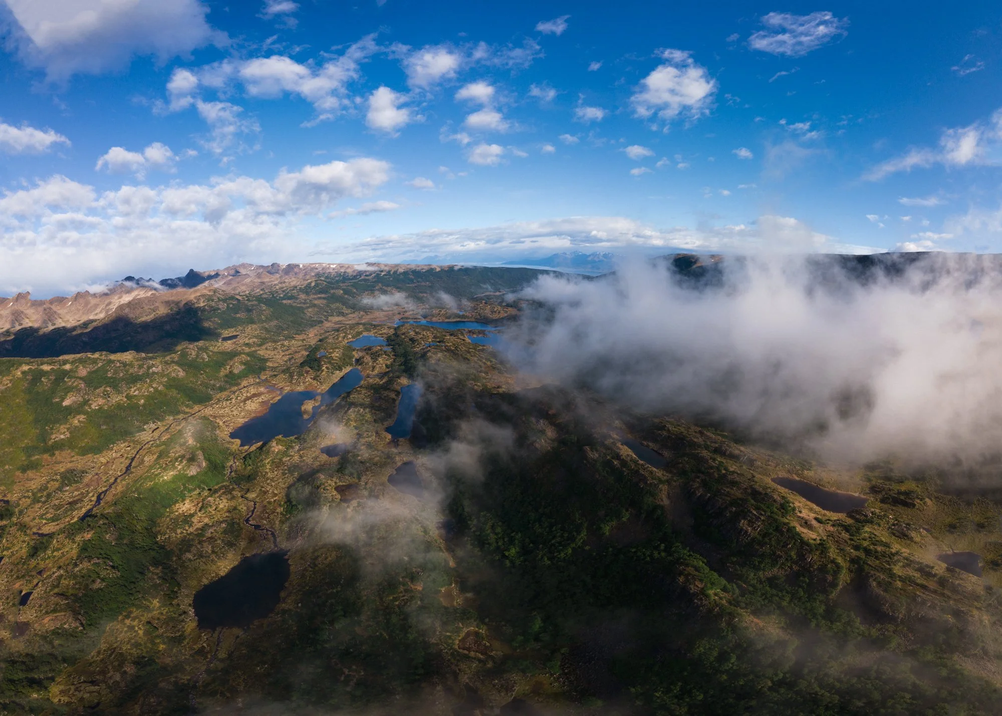 Aerial view of a mountainous landscape with lakes, clouds, and clear blue sky.