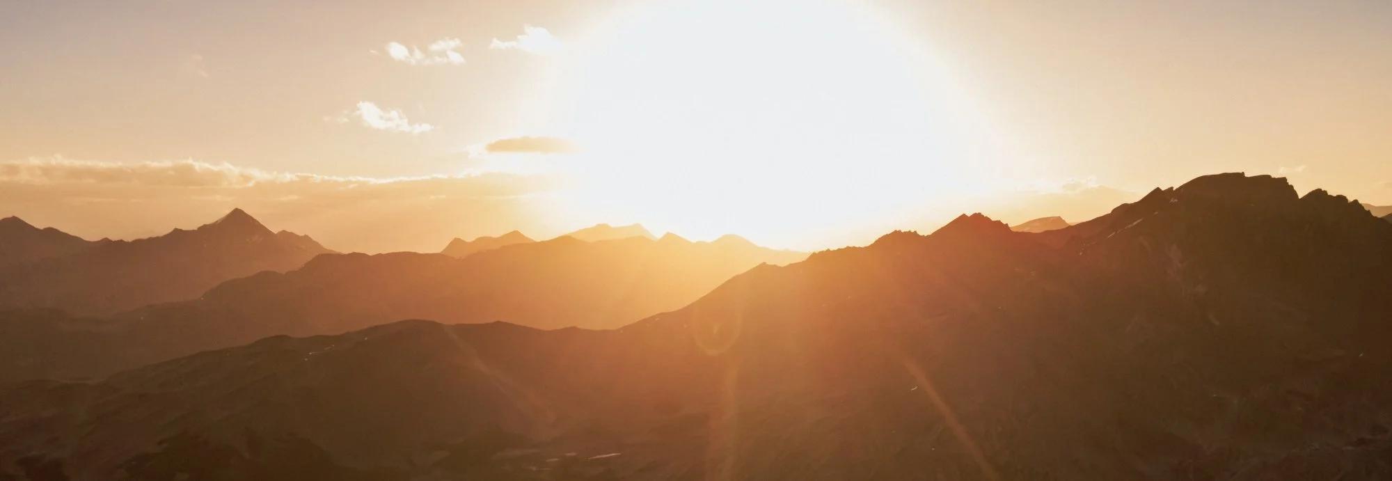Sunset over mountain range with golden light and scattered clouds.