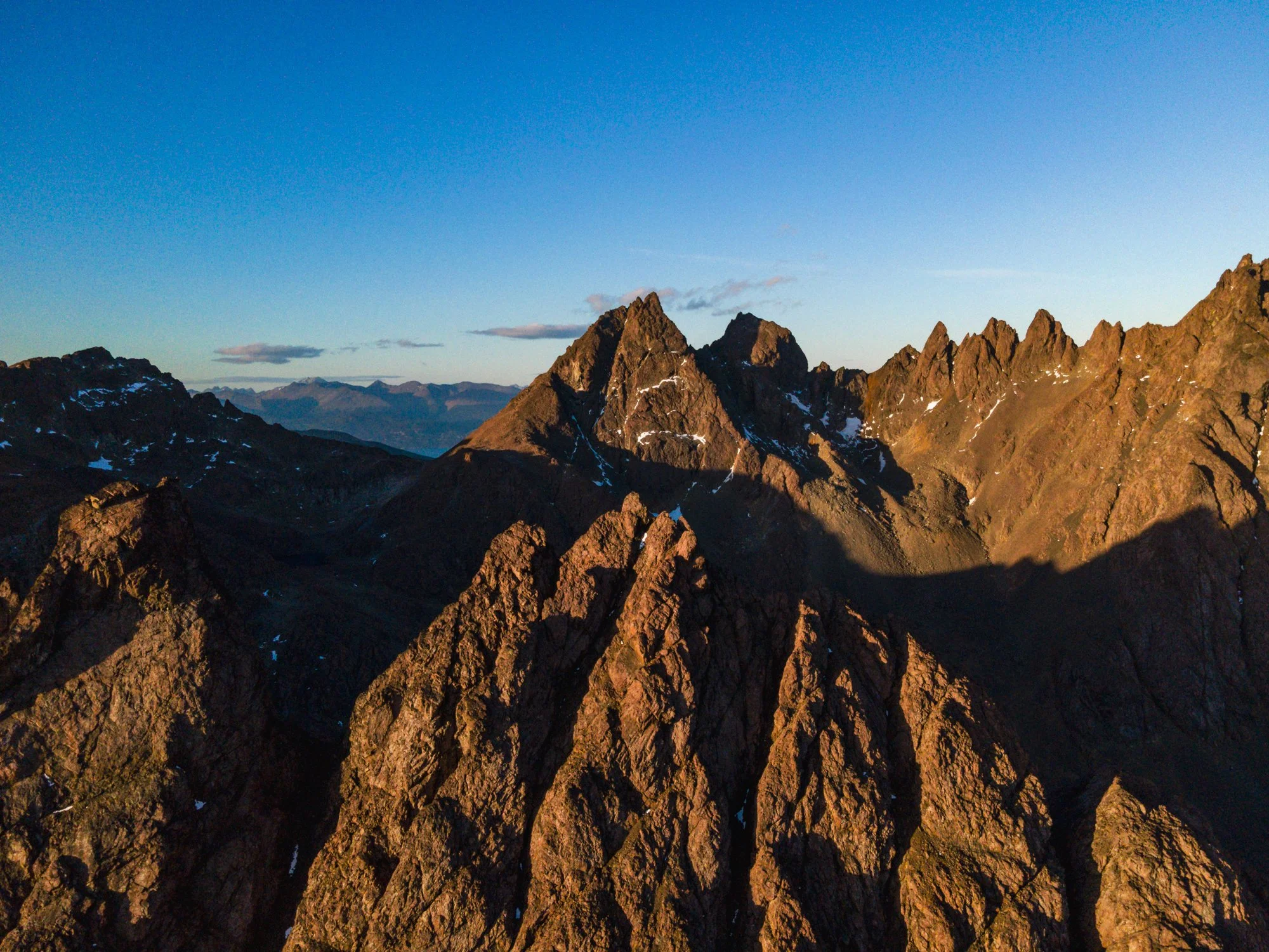 View of rugged mountain peaks with patches of snow under a clear blue sky.