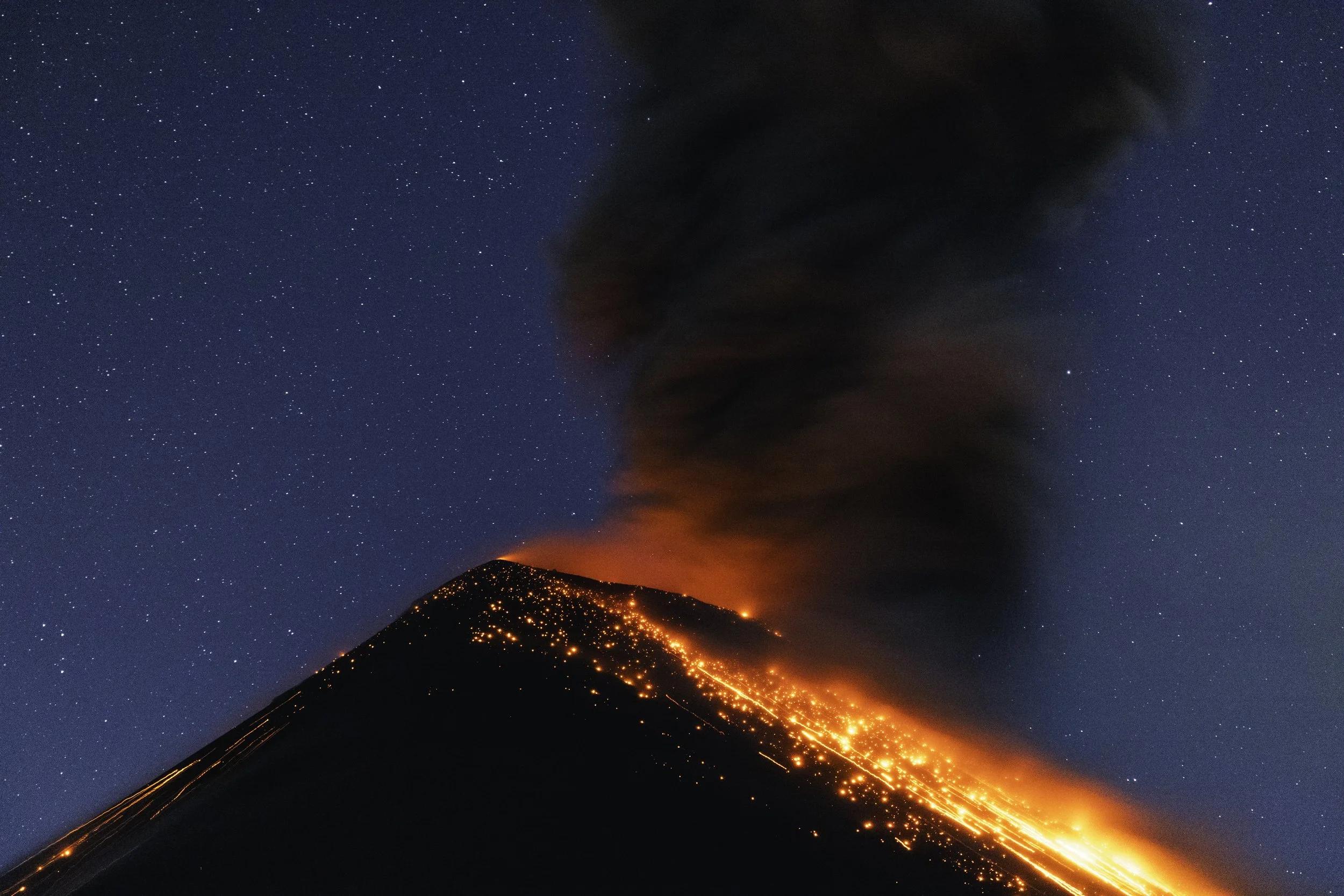 A volcano erupting at night with glowing lava flowing down its sides and dark smoke billowing into the starry sky.