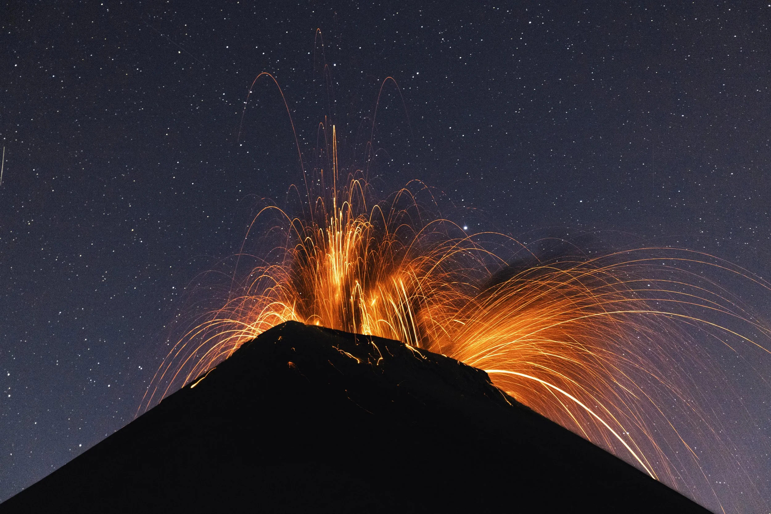 Erupting volcano spewing lava and ash with a starry night sky in the background.